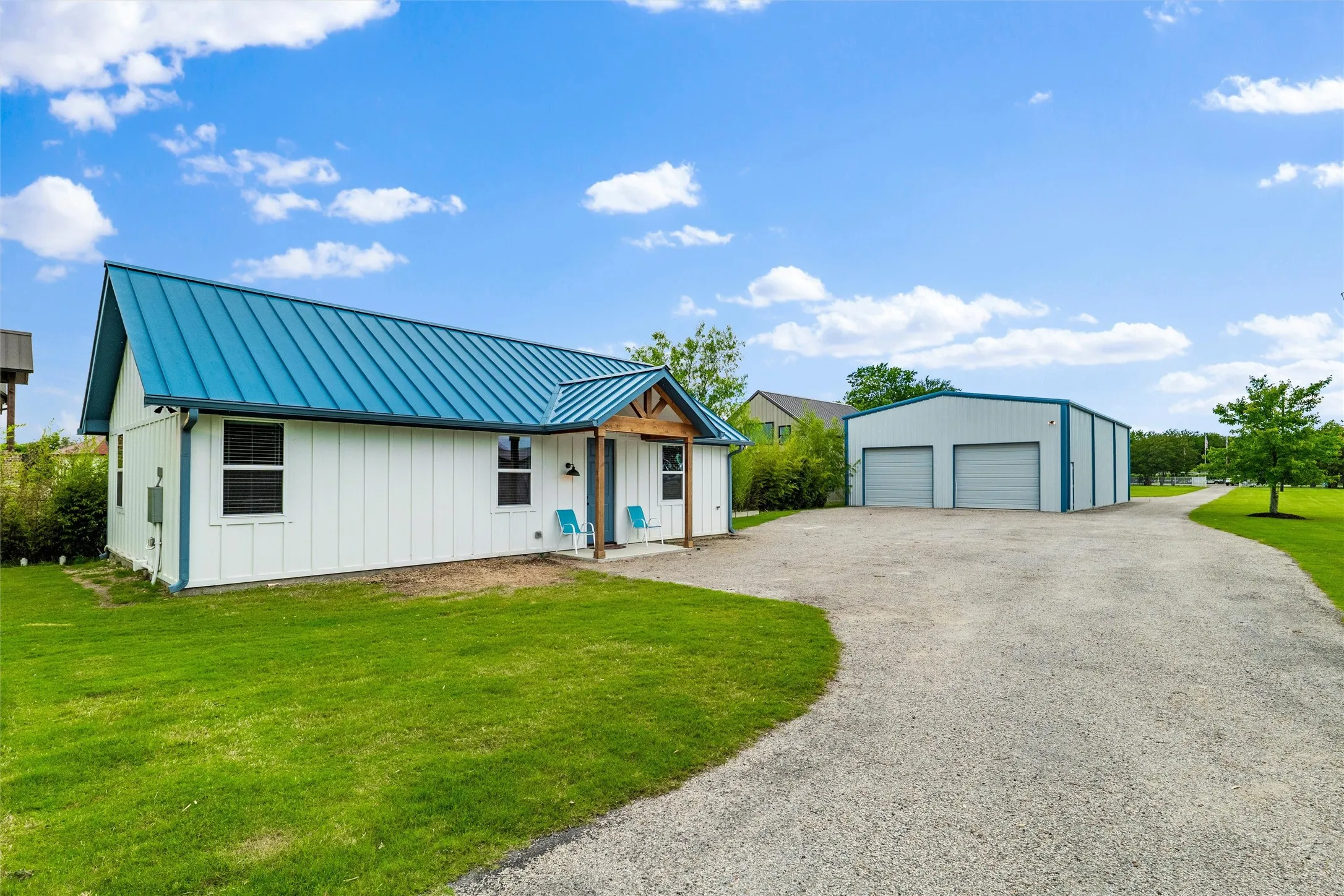 Guest house and detached garage are positioned side by side with gravel driveway access extending throughout the exterior approach. Guest house features board and batten siding, covered front entry, exposed beam accents, and surrounding landscaped lawn areas.