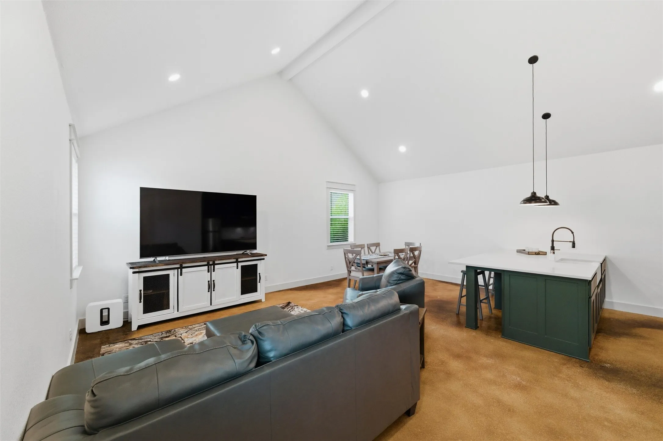 Guest house features vaulted ceilings, recessed lighting, open-concept living and dining area, spacious kitchen island with seating, large windows for natural light, and polished concrete flooring throughout.