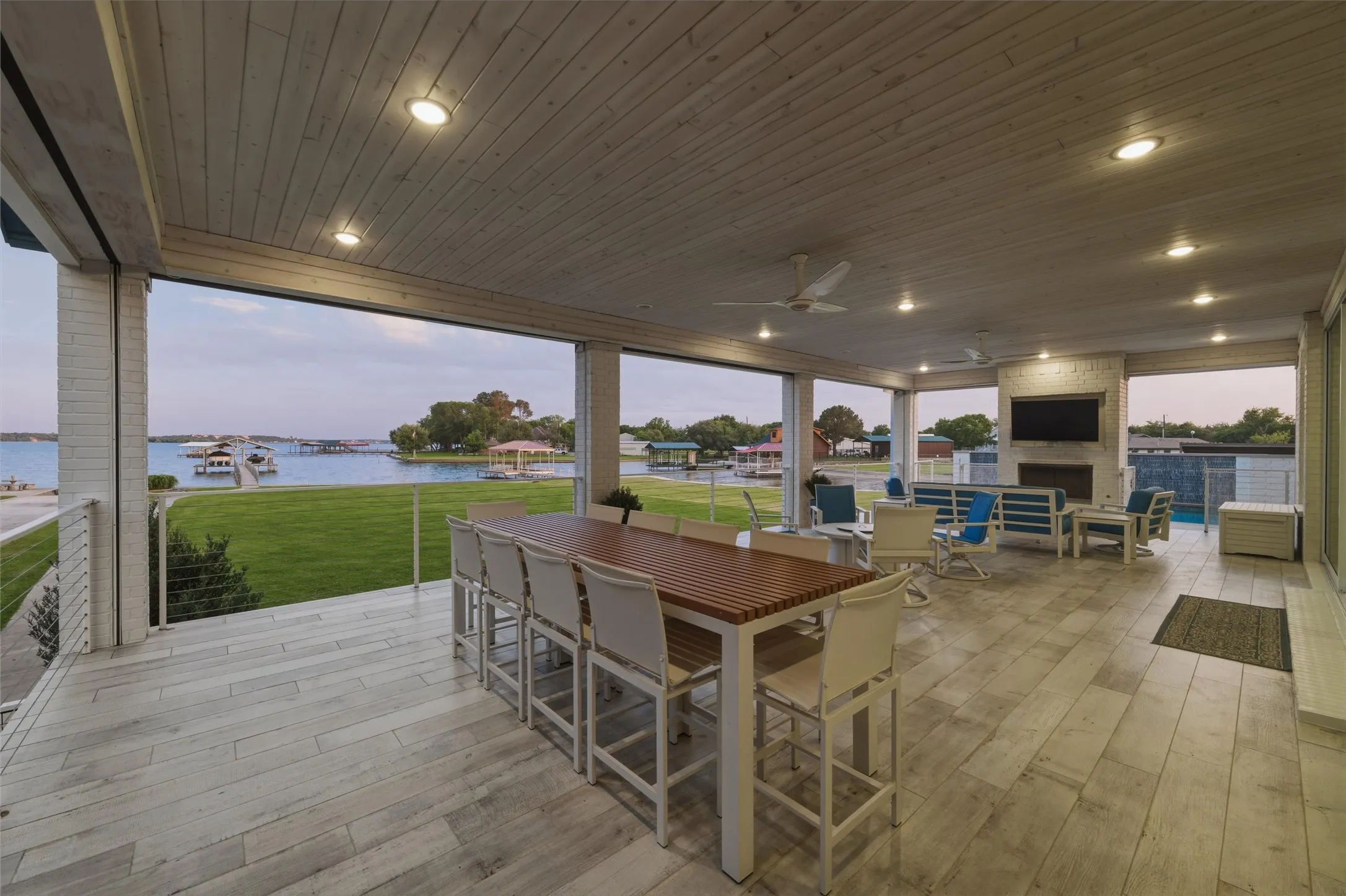 Covered patio includes outdoor dining and gathering areas with direct connection to the interior living spaces through sliding glass doors. Waterfront views extend across the lawn and shoreline areas beyond the covered exterior space.