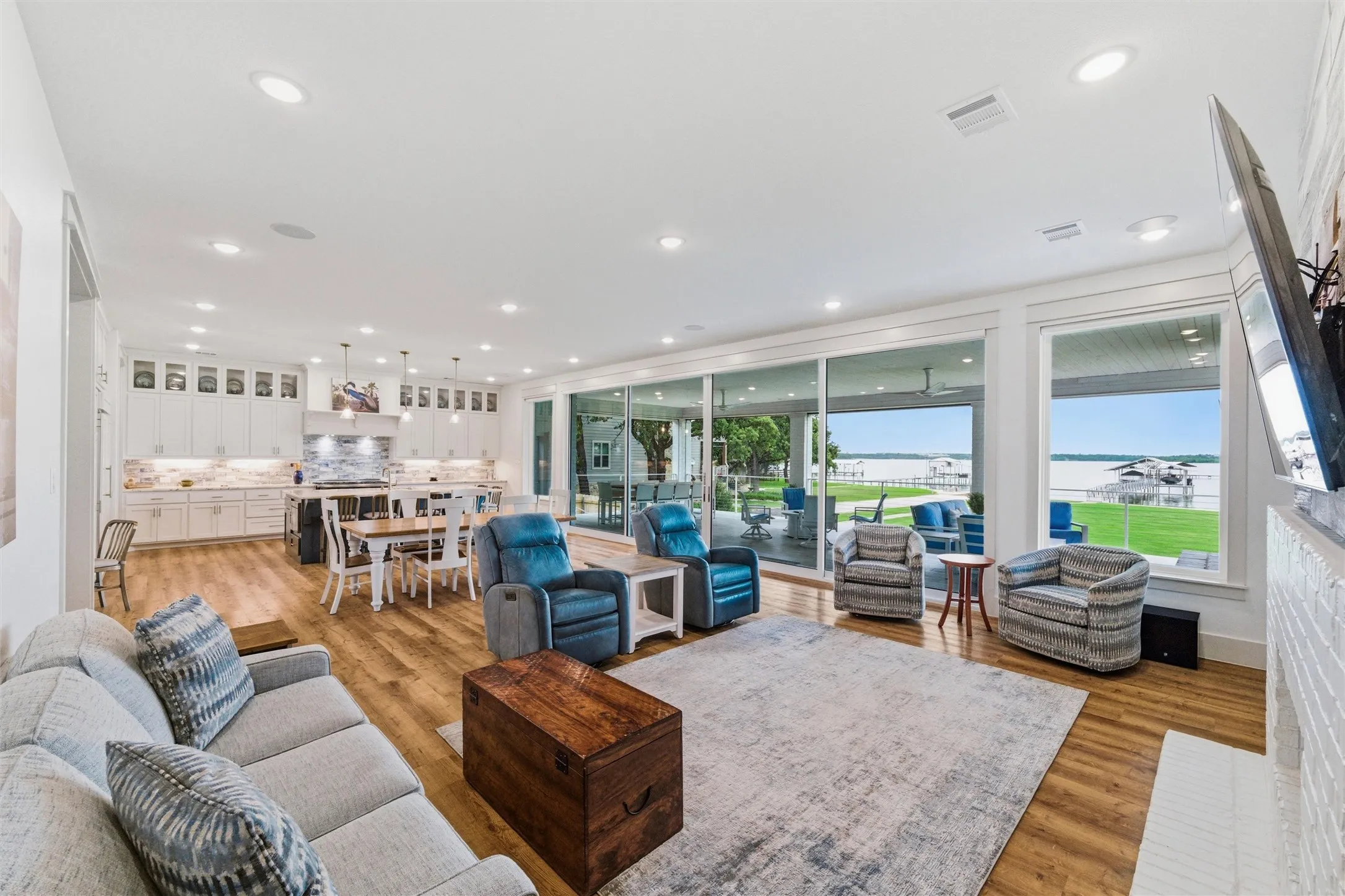 Living room overlooks the waterfront setting through expansive sliding glass doors and large windows. Open layout provides direct flow into the kitchen and dining areas while maintaining clear sightlines throughout the main living spaces.