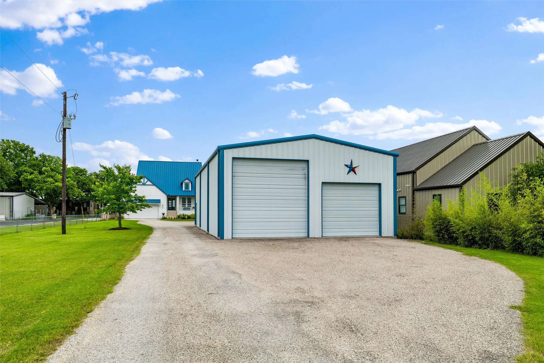Detached garage features dual overhead garage doors, extended gravel driveway access, vertical siding detail, and surrounding lawn areas positioned separately from the main residence.