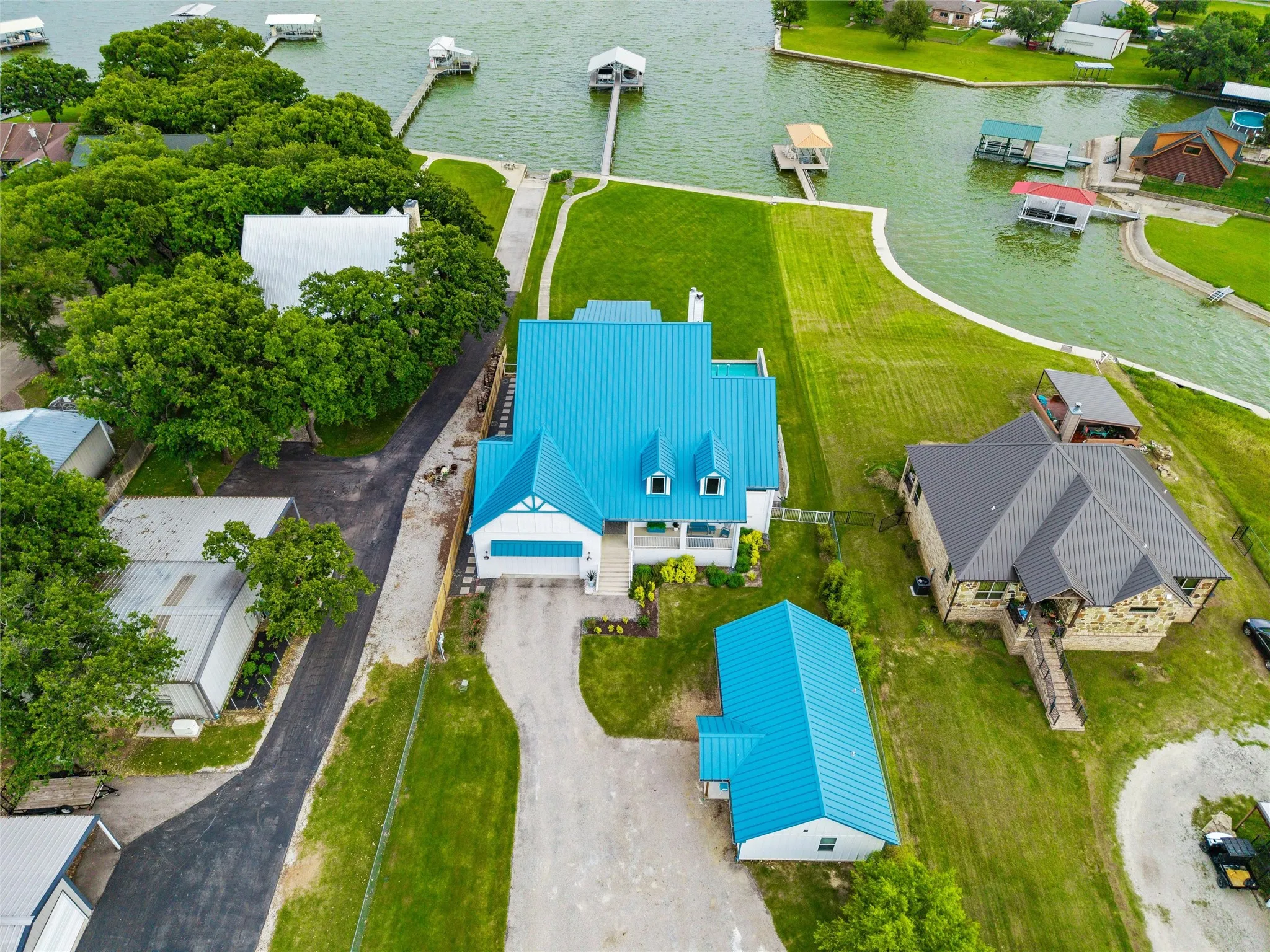 Aerial view showcases direct shoreline access with private dock extending into the lake. Main residence, guest house, detached garage, landscaped lawn areas, and waterfront improvements are visible throughout the property boundaries.