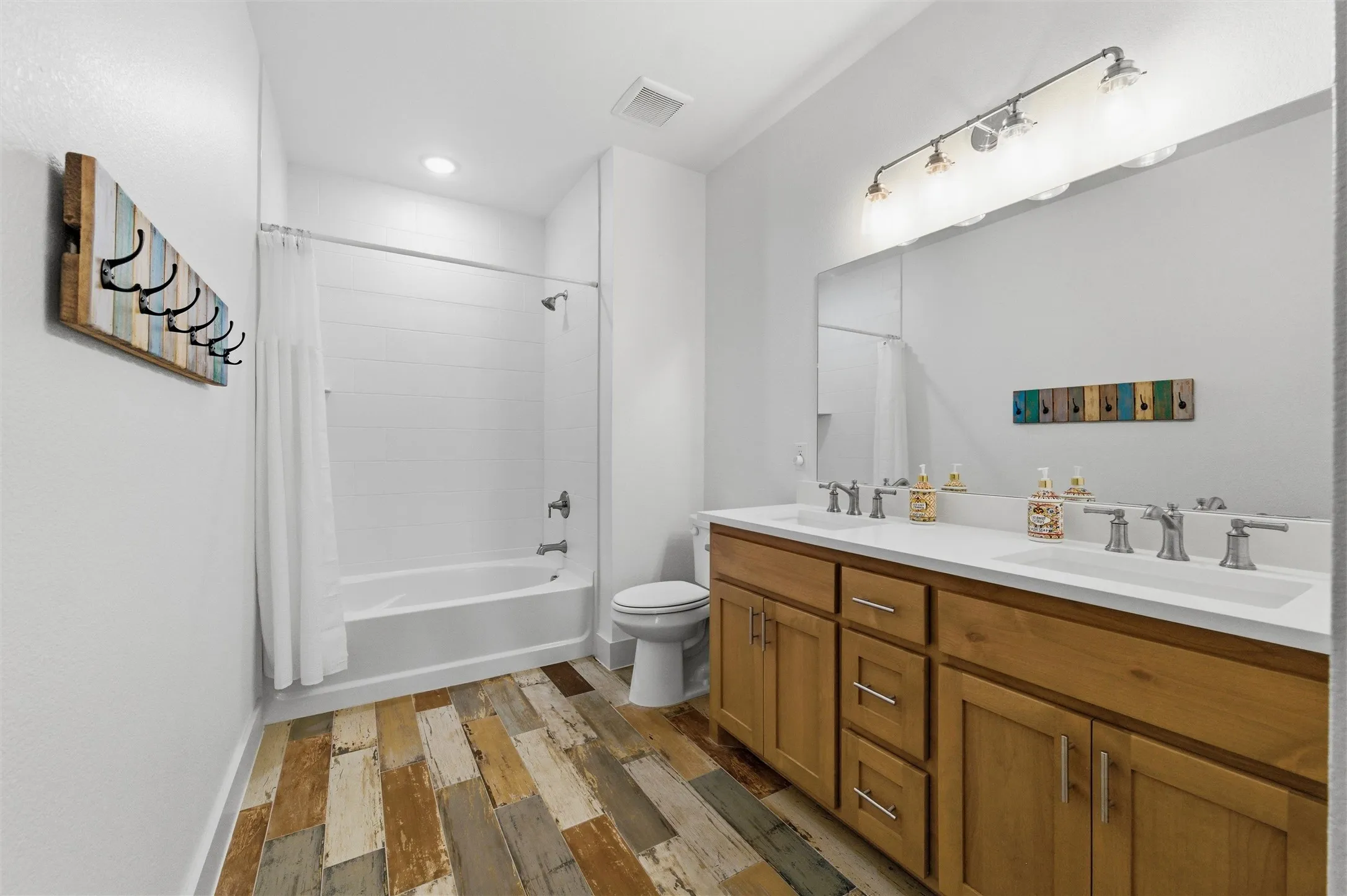 Secondary bathroom features dual sinks with extended vanity space, tub and shower combination with tiled surround, decorative flooring detail, and neutral finishes throughout.