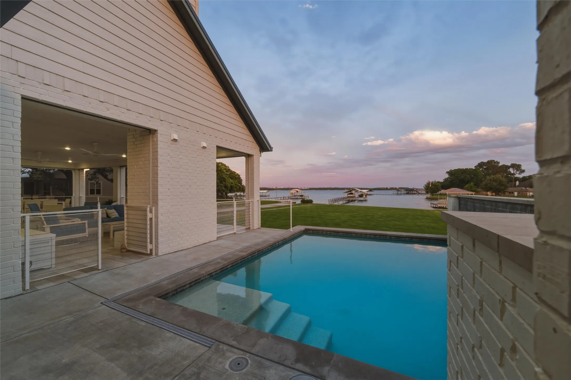 Pool area features in-ground rectangular pool with integrated entry steps, surrounding deck space, painted brick privacy walls, and open waterfront views extending across the rear lawn area. Covered patio spaces connect directly to the pool and outdoor living areas.