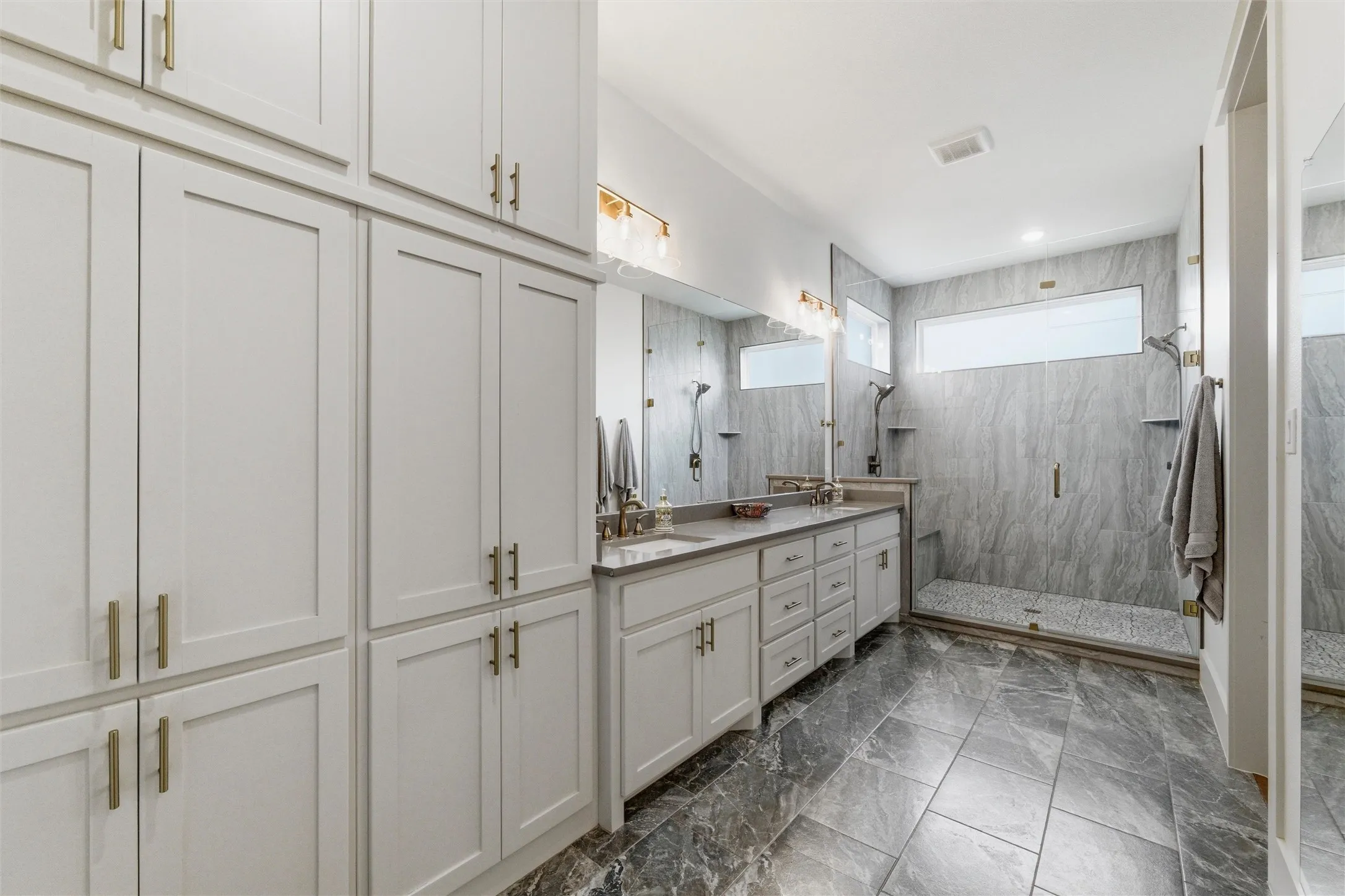Primary bathroom features expansive walk-in shower with dual shower heads, built-in bench seating, full glass enclosure, and dual-sink vanity with extensive cabinetry storage. Large transom windows provide natural light while maintaining privacy throughout the space.
