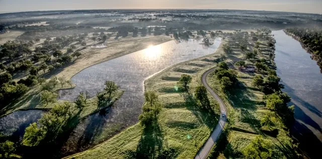 Expansive aerial landscape featuring a prominent river, a winding paved road, and a reflective body of water