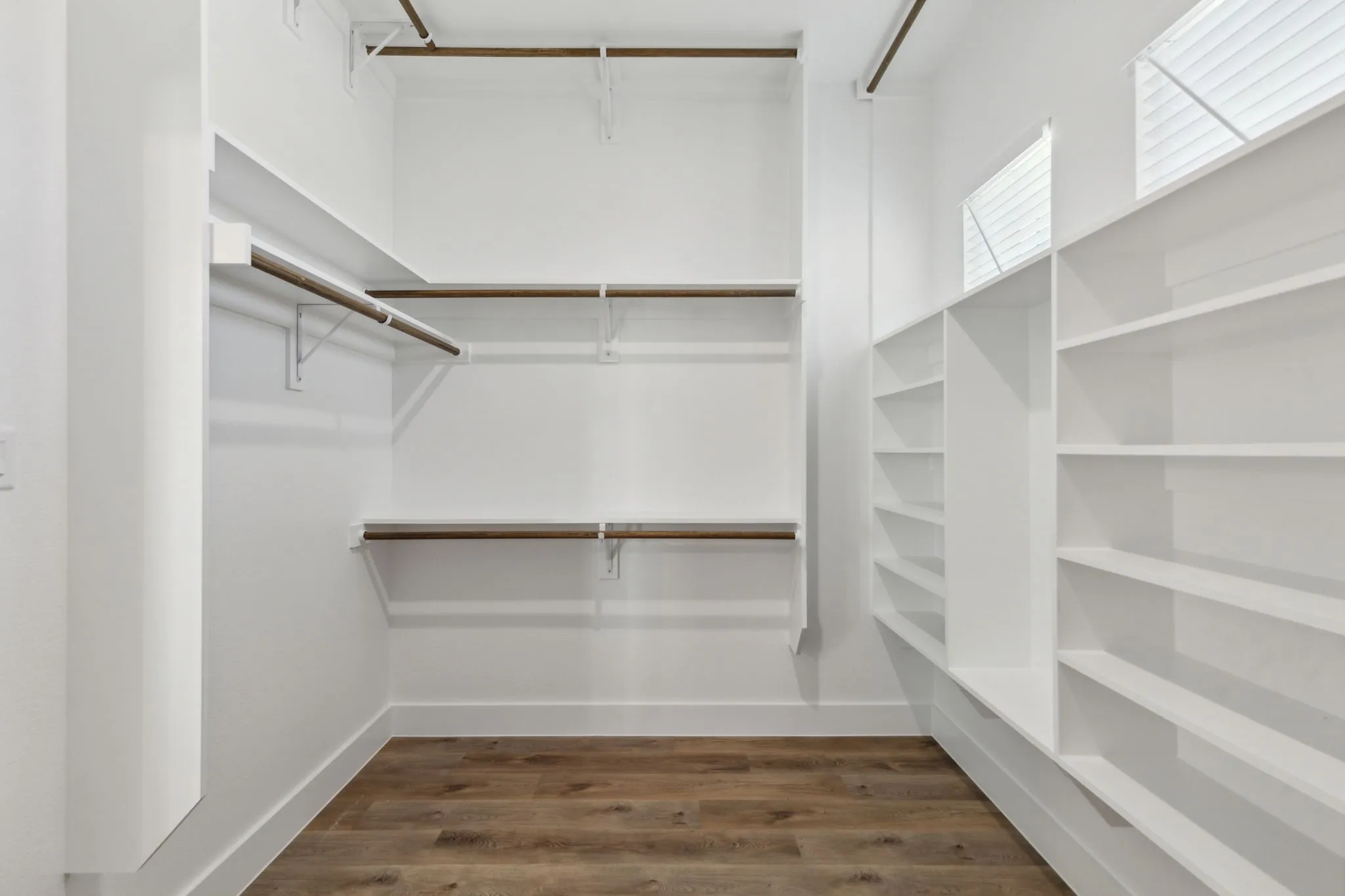 Spacious walk-in closet featuring wood-finish flooring, white walls, built-in shelving, hanging rods, and integrated windows with blinds
