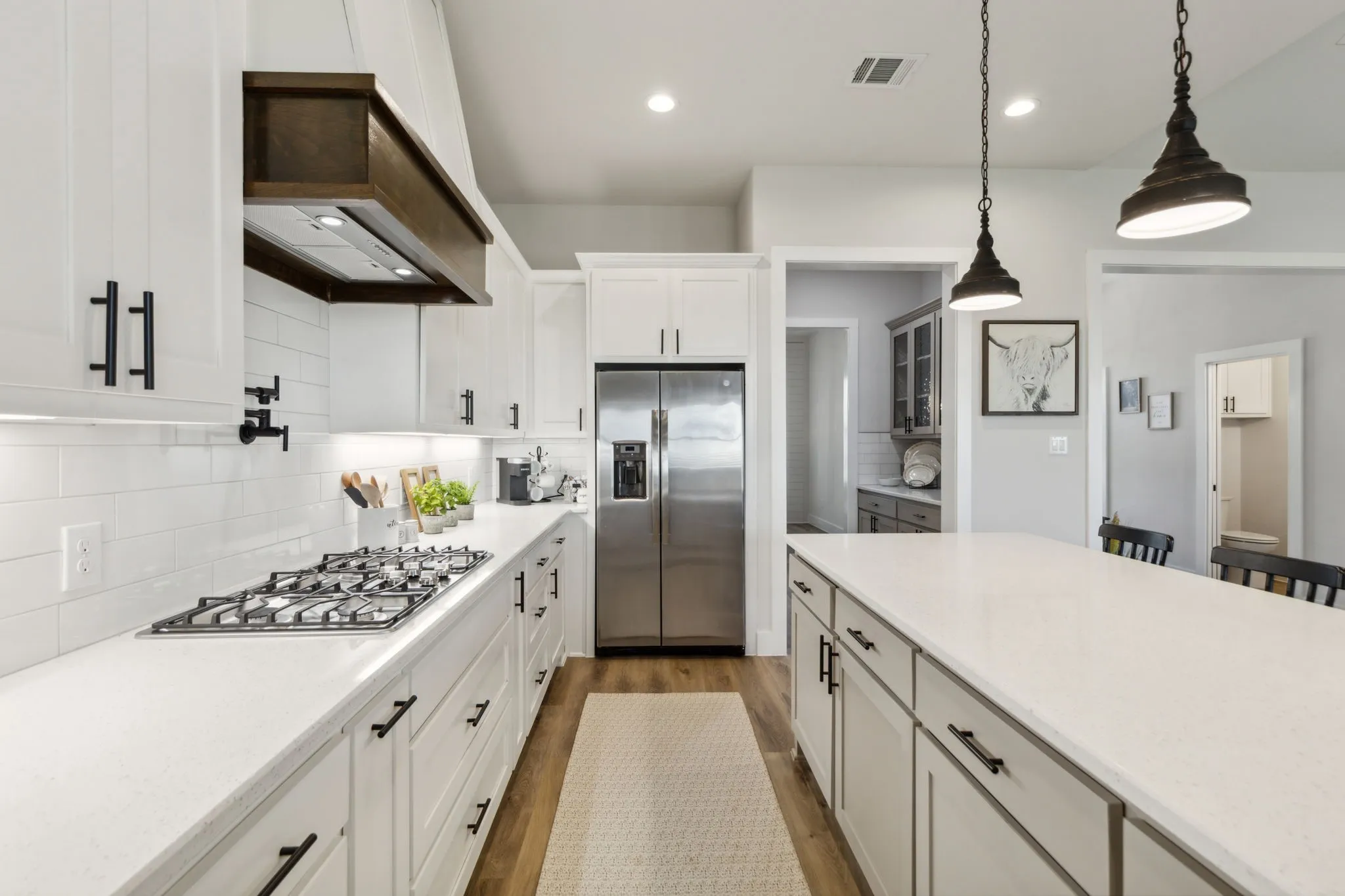 Contemporary kitchen featuring a gas cooktop, stainless steel refrigerator, white subway tile backsplash, white cabinetry with black hardware, and a large island with pendant lighting