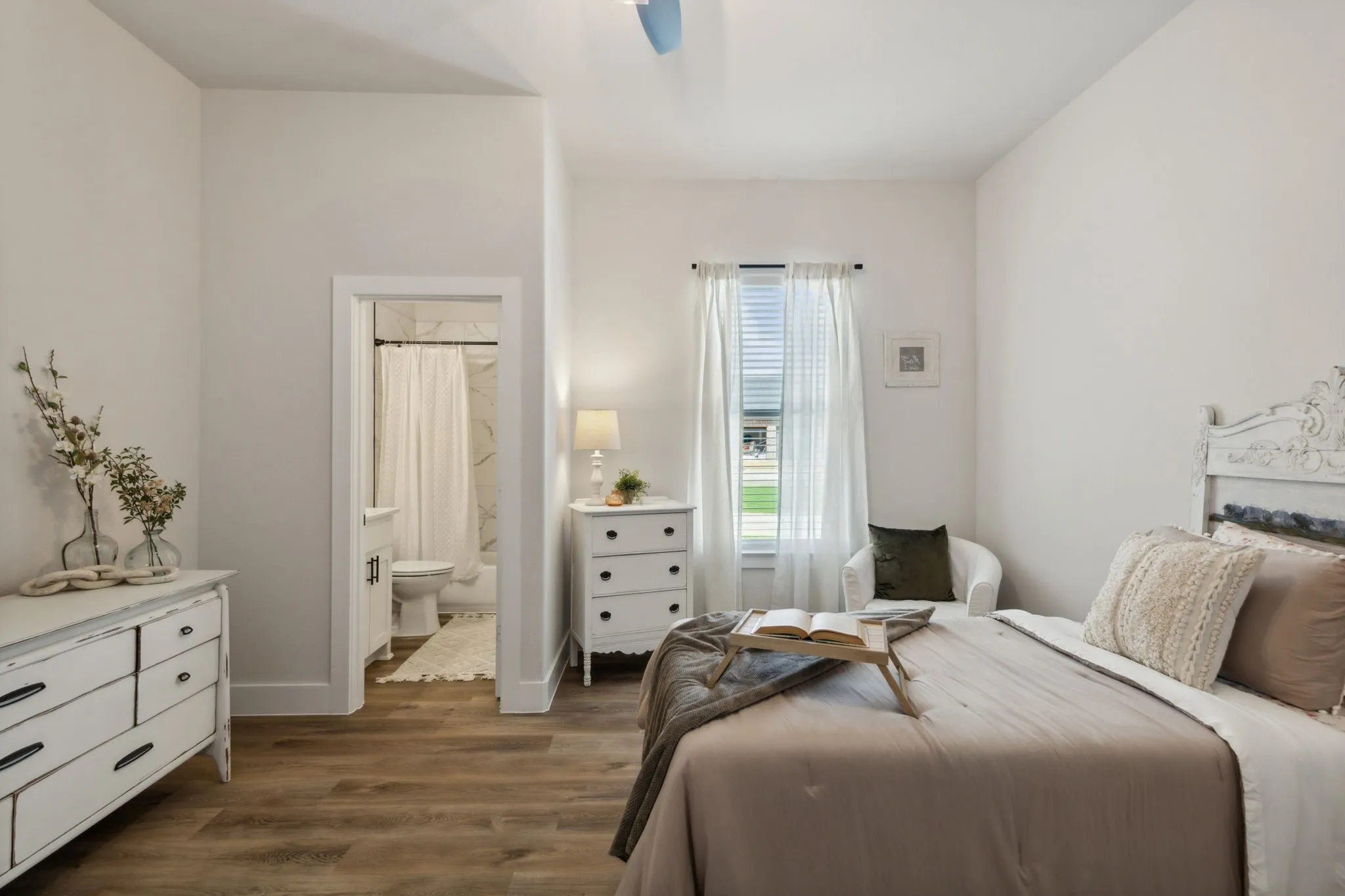 Bedroom featuring wood-finish flooring, a white headboard with carved details, and a window with blinds and sheer curtains