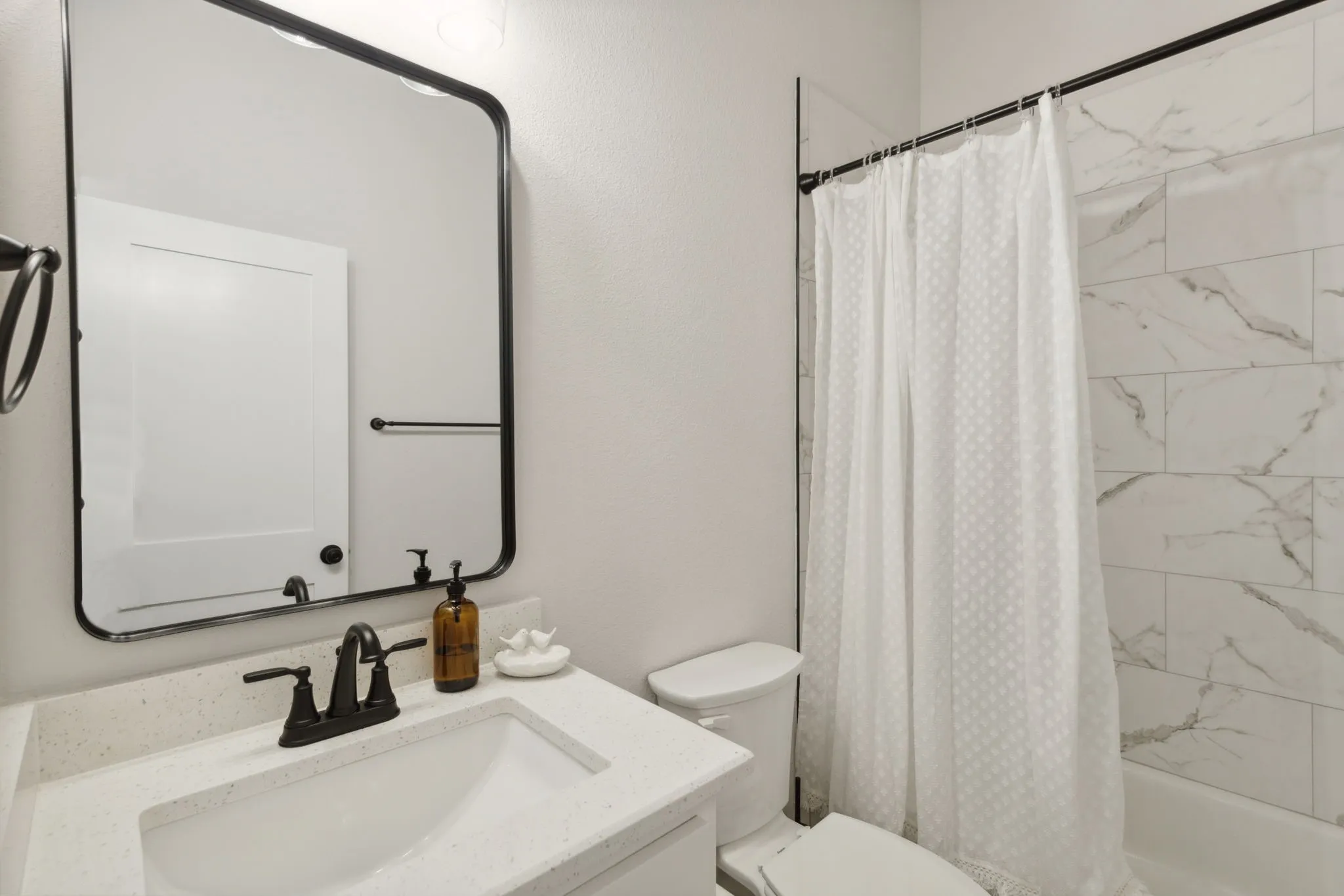 Bathroom featuring an undermount sink, a light-toned countertop, a black-framed mirror, a black faucet, and white subway tile in the shower