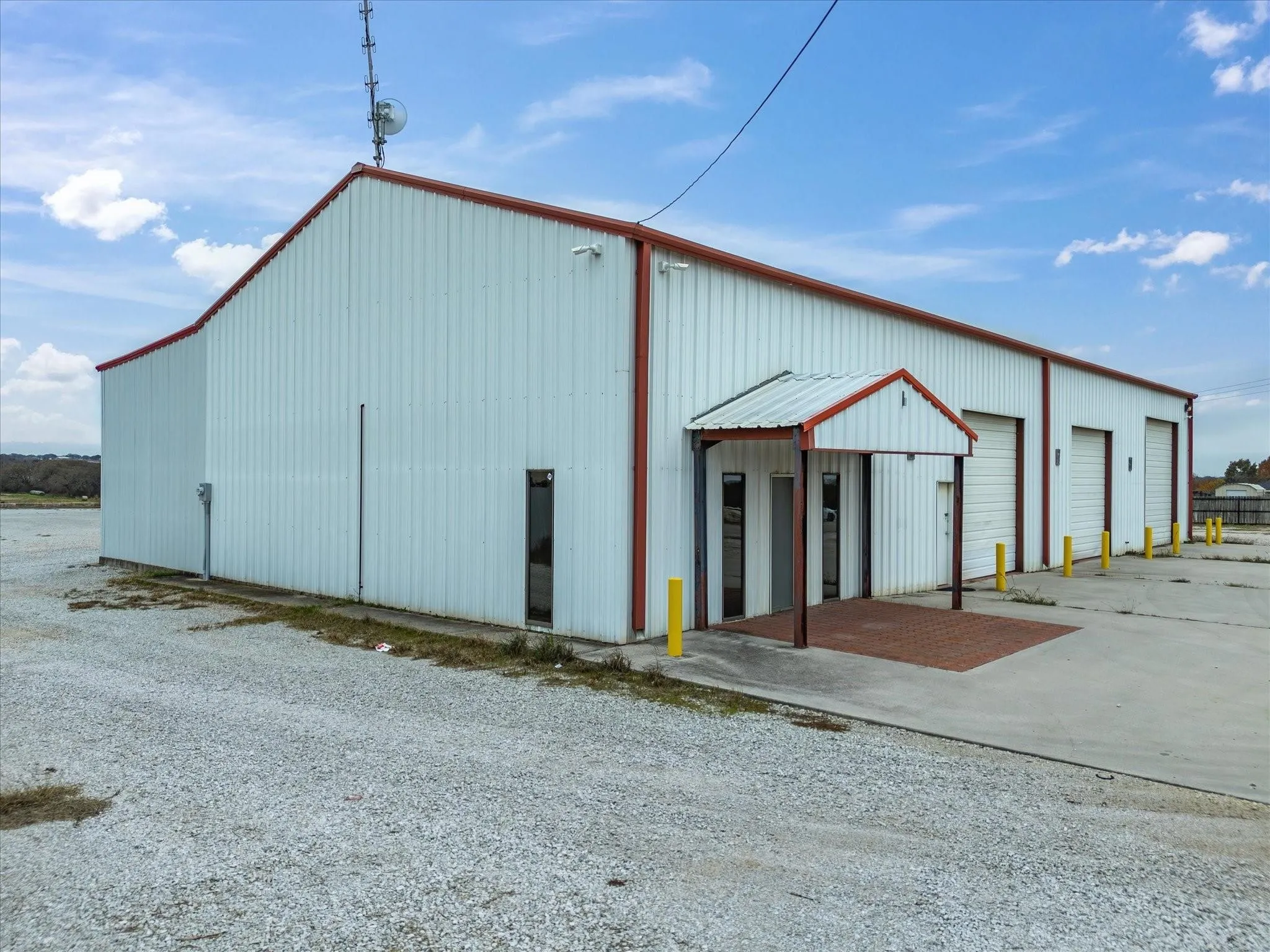 Commercial building featuring a white corrugated metal exterior, red trim, and multiple roll-up doors