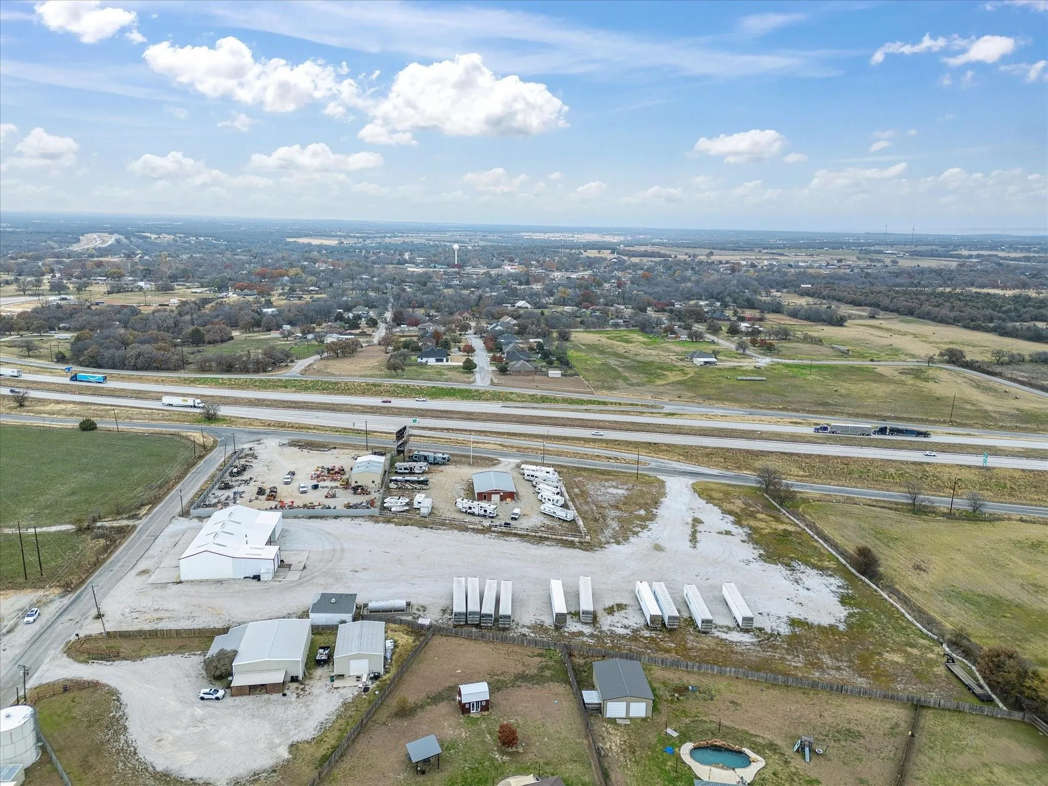 Expansive commercial property featuring multiple structures, direct highway frontage, large gravel parking areas, and open land