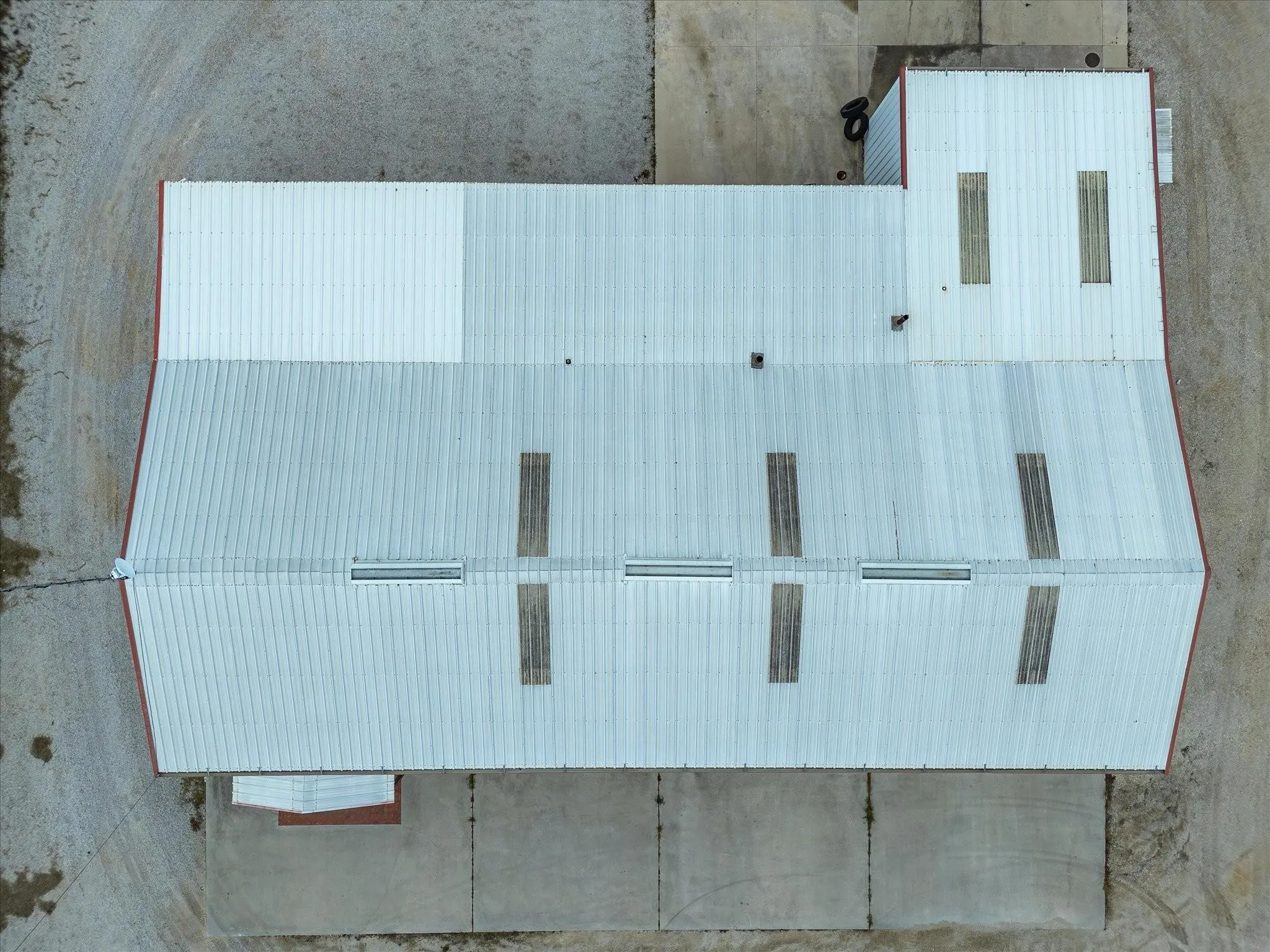 Metal roof structure featuring light-colored corrugated panels, multiple skylights, and red trim accents