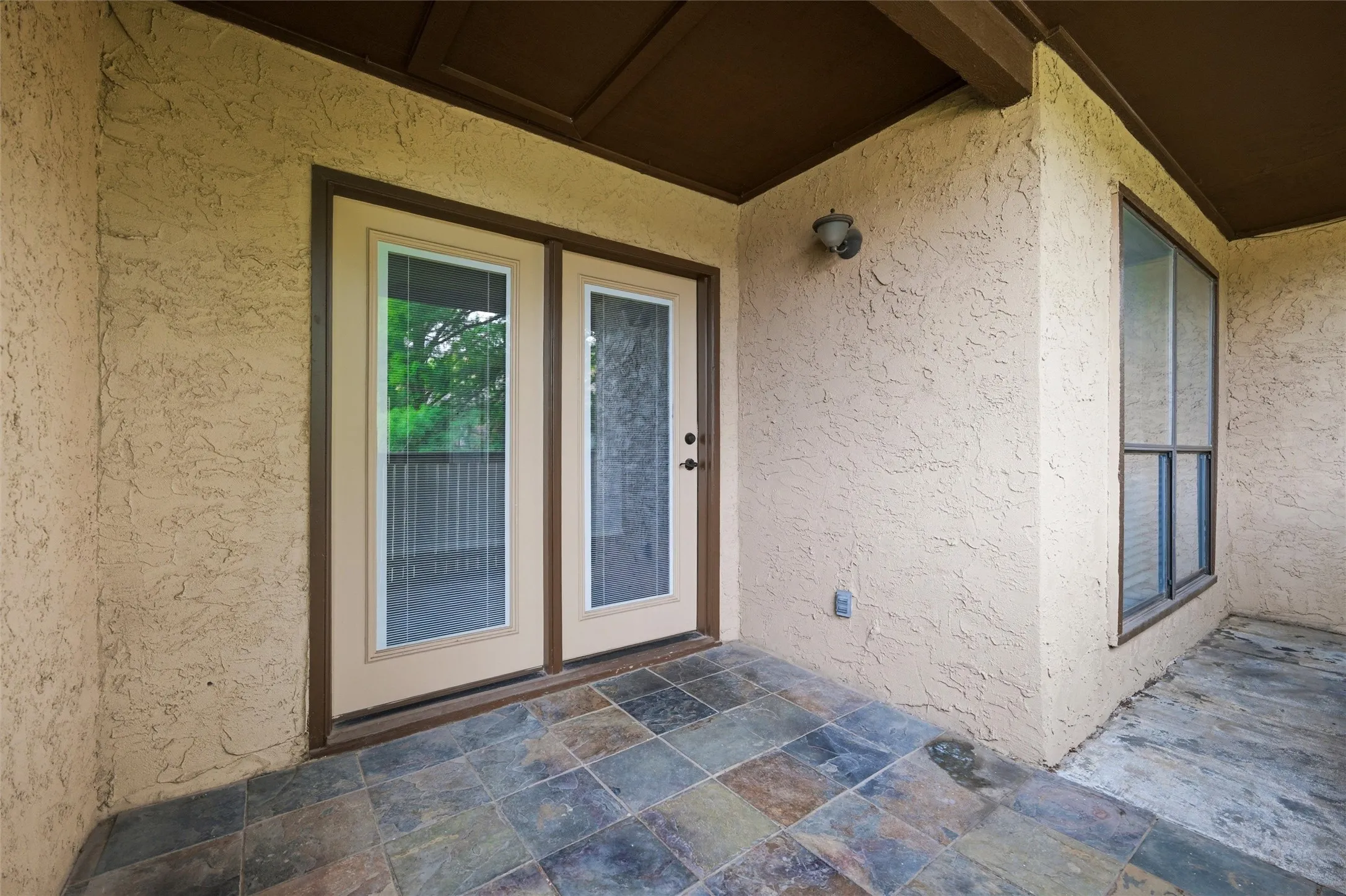 Outdoor patio featuring multi-toned slate-look tile flooring, textured stucco walls, and a recessed ceiling with exposed beams