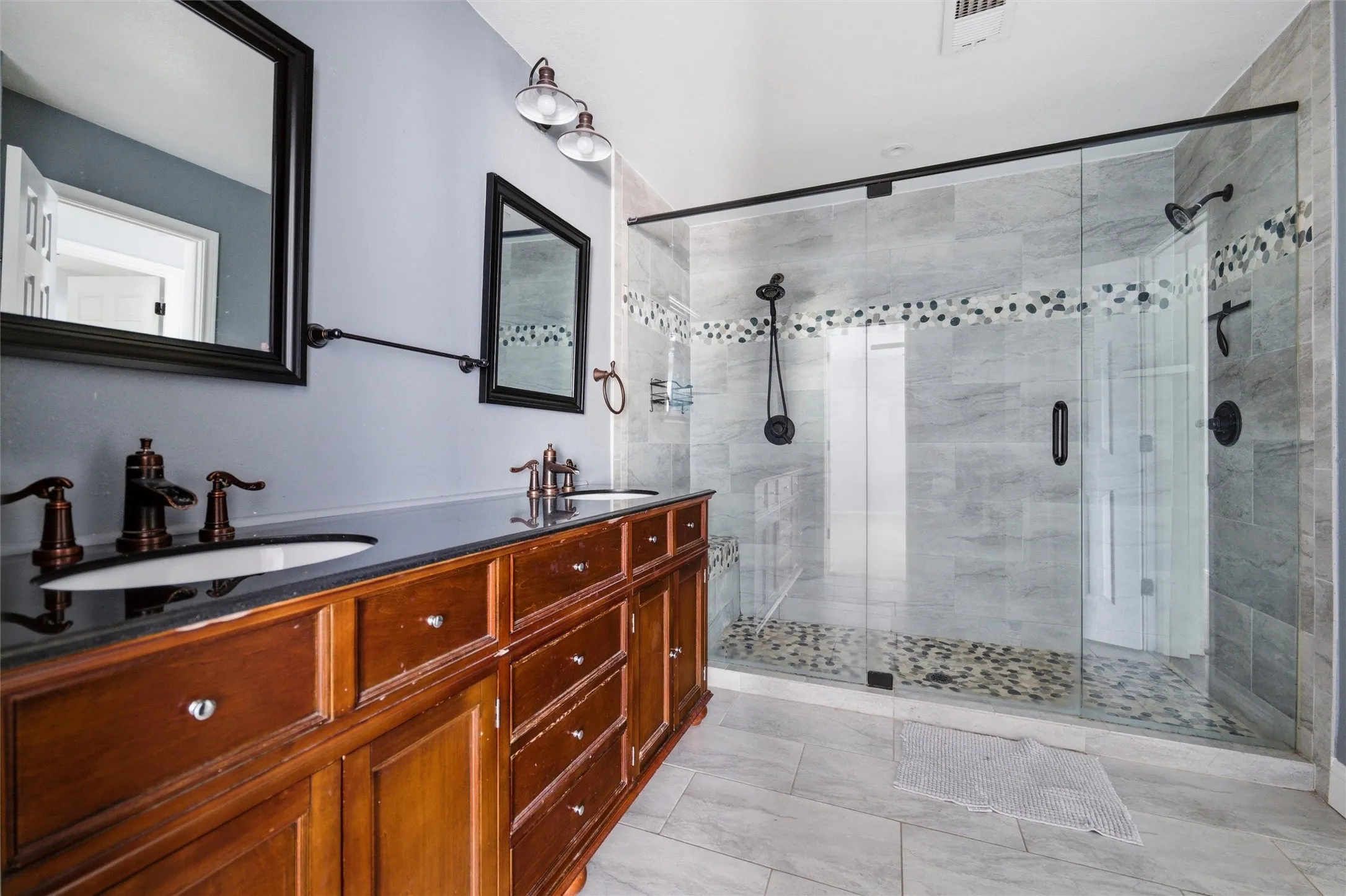 Dual sink vanity with dark wood cabinetry and black countertops