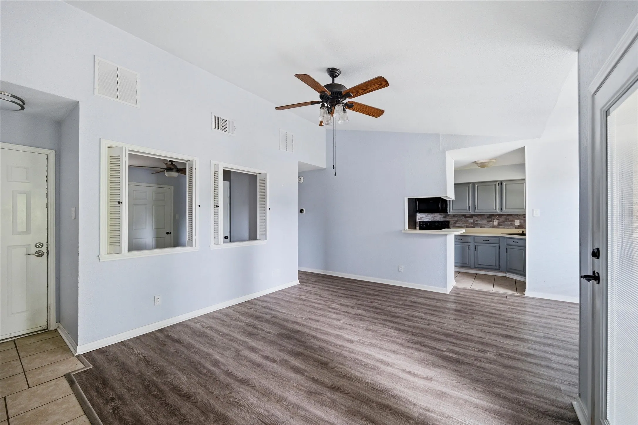 Living area featuring wood-finish flooring, a ceiling fan, and a pass-through window to the kitchen