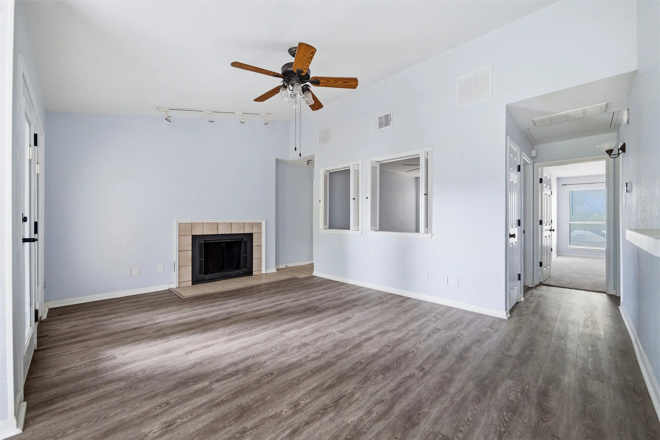 Living area with wood-finish flooring, a tile-surround fireplace, and a ceiling fan