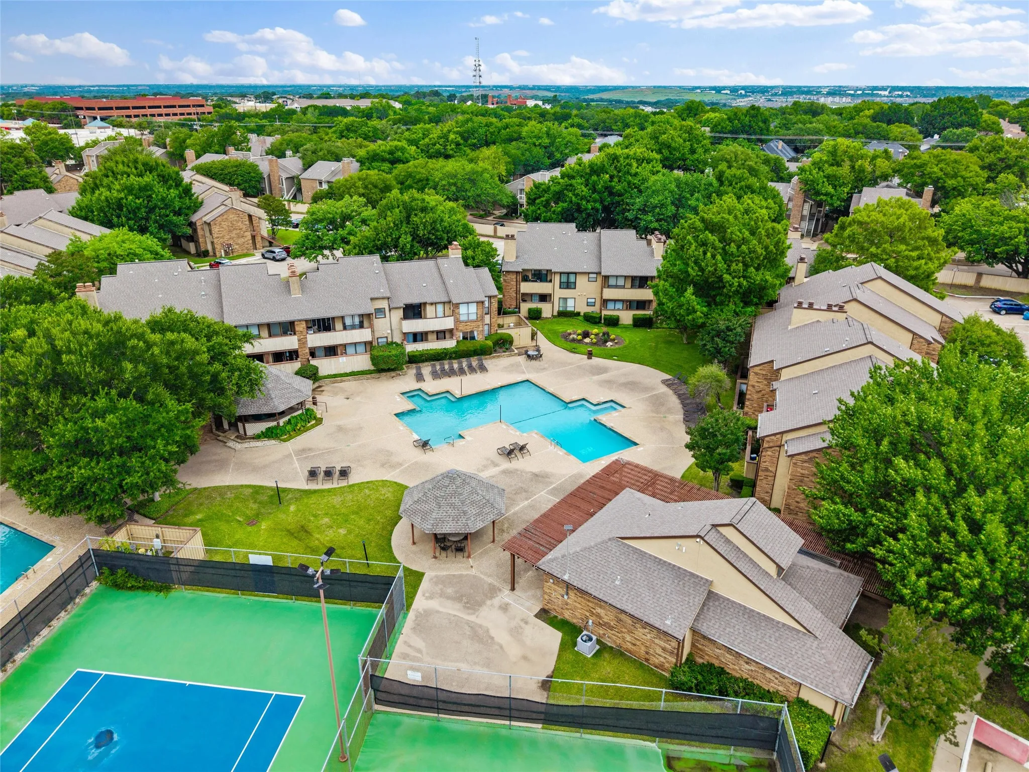 Expansive aerial view showcasing multiple residential buildings, a central swimming pool with surrounding concrete patio, and a separate tennis court