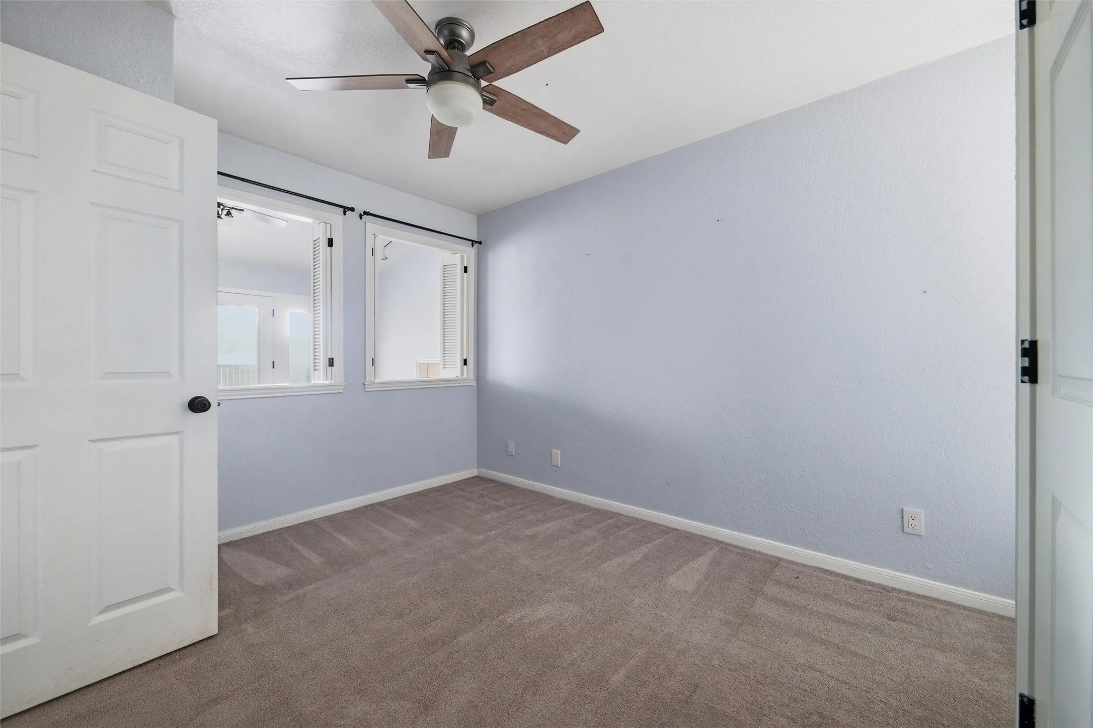 Carpeted interior room featuring light blue walls, two transom windows with dark hardware, and a ceiling fan with integrated lighting