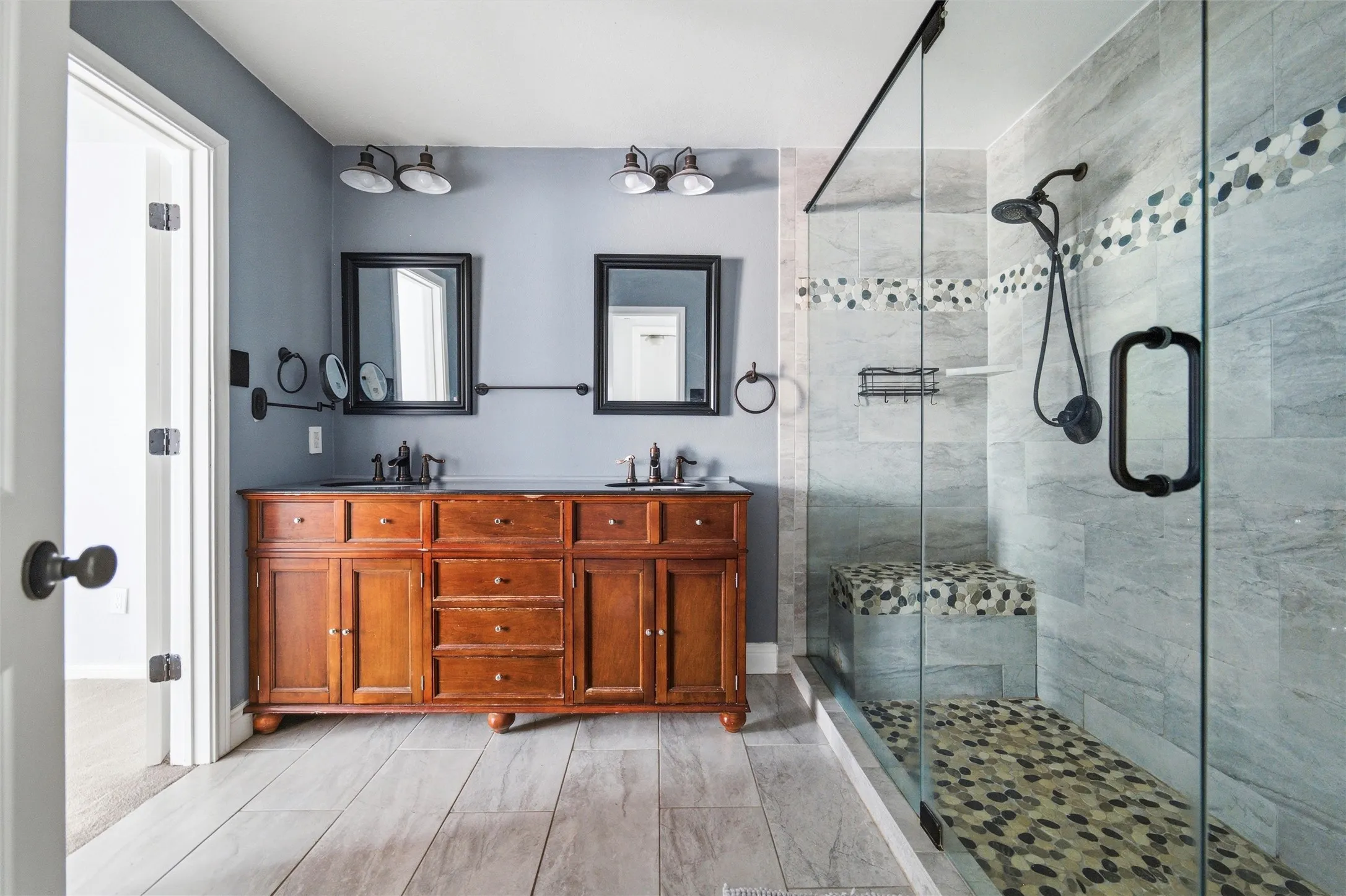 Spacious bathroom featuring a dual vanity with a rich wood finish, dual mirrors, and contemporary lighting