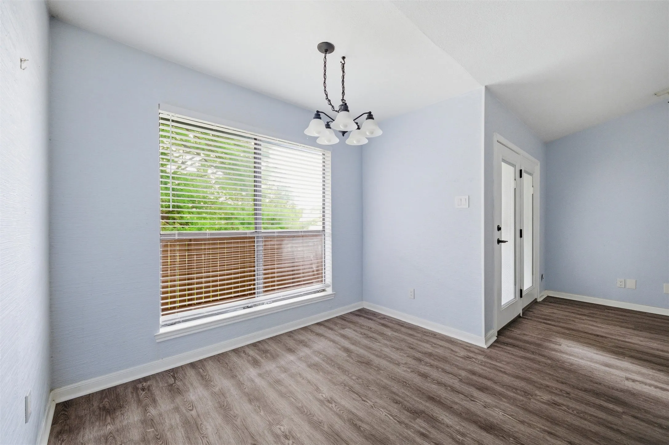 Interior room featuring wood-finish flooring, light blue wall paint, and a multi-light chandelier