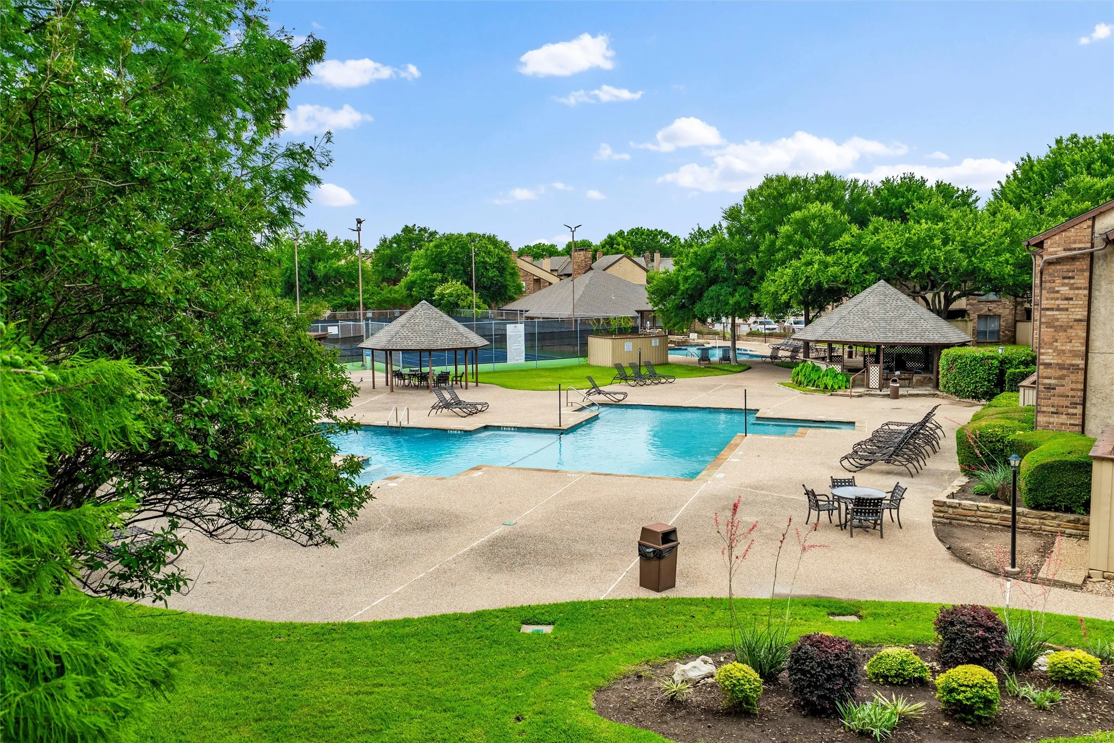 Expansive swimming pool area featuring a perimeter deck, multiple shaded gazebos, and a tennis court