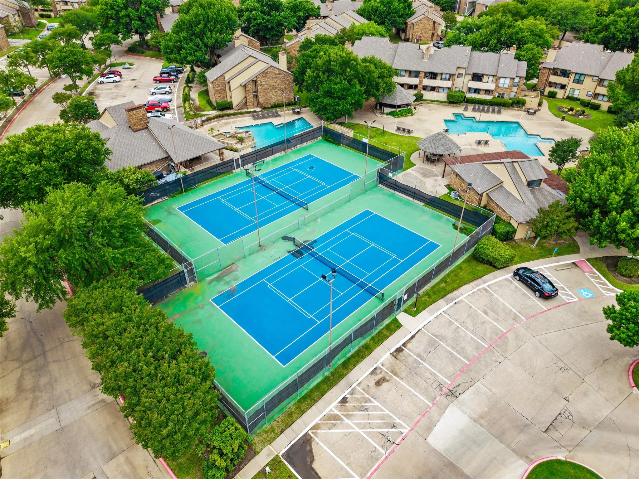 Two full-size tennis courts with blue playing surfaces and green surrounds