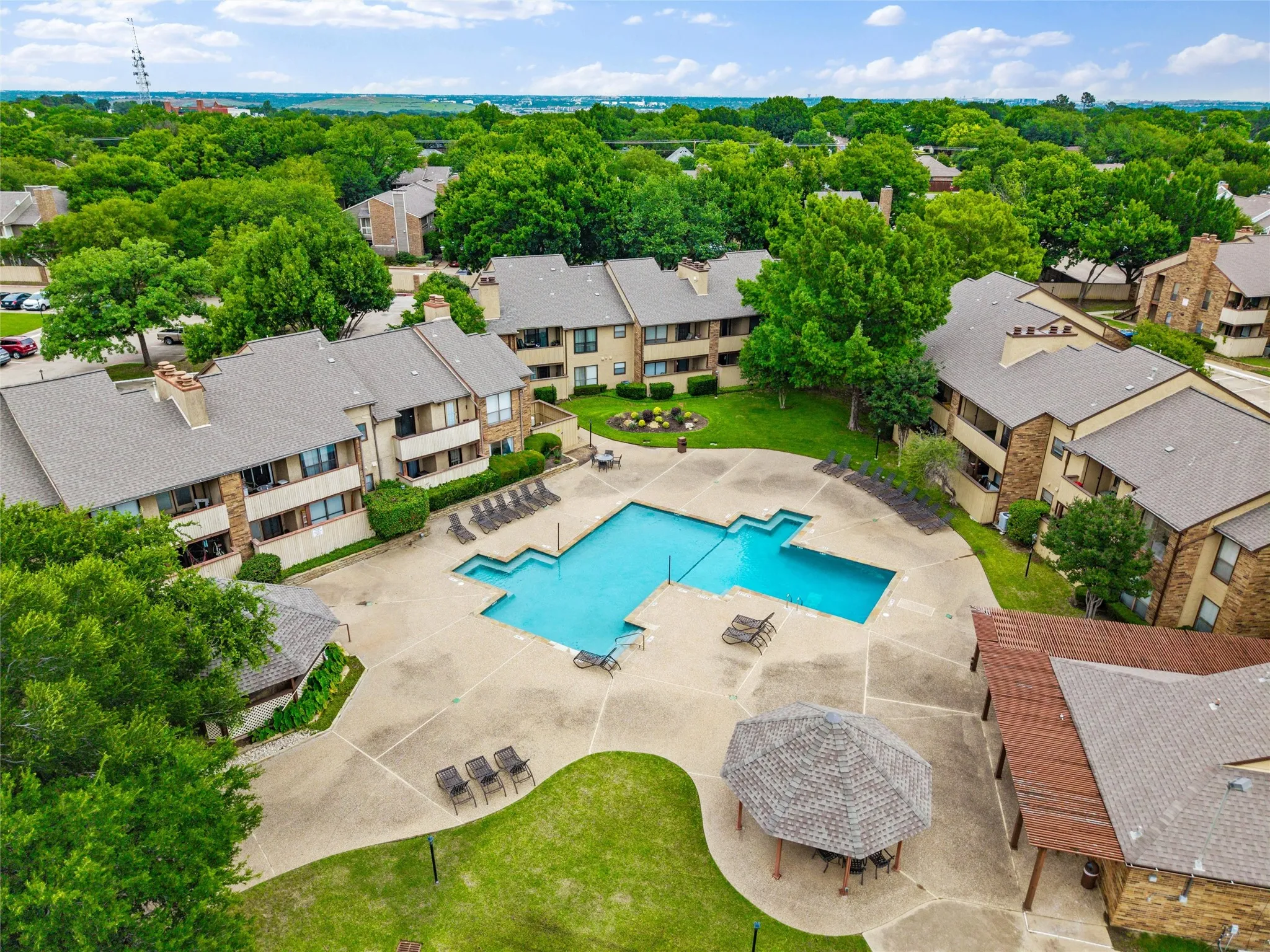 Community pool with extensive concrete decking, surrounded by multi-story residential buildings and mature trees