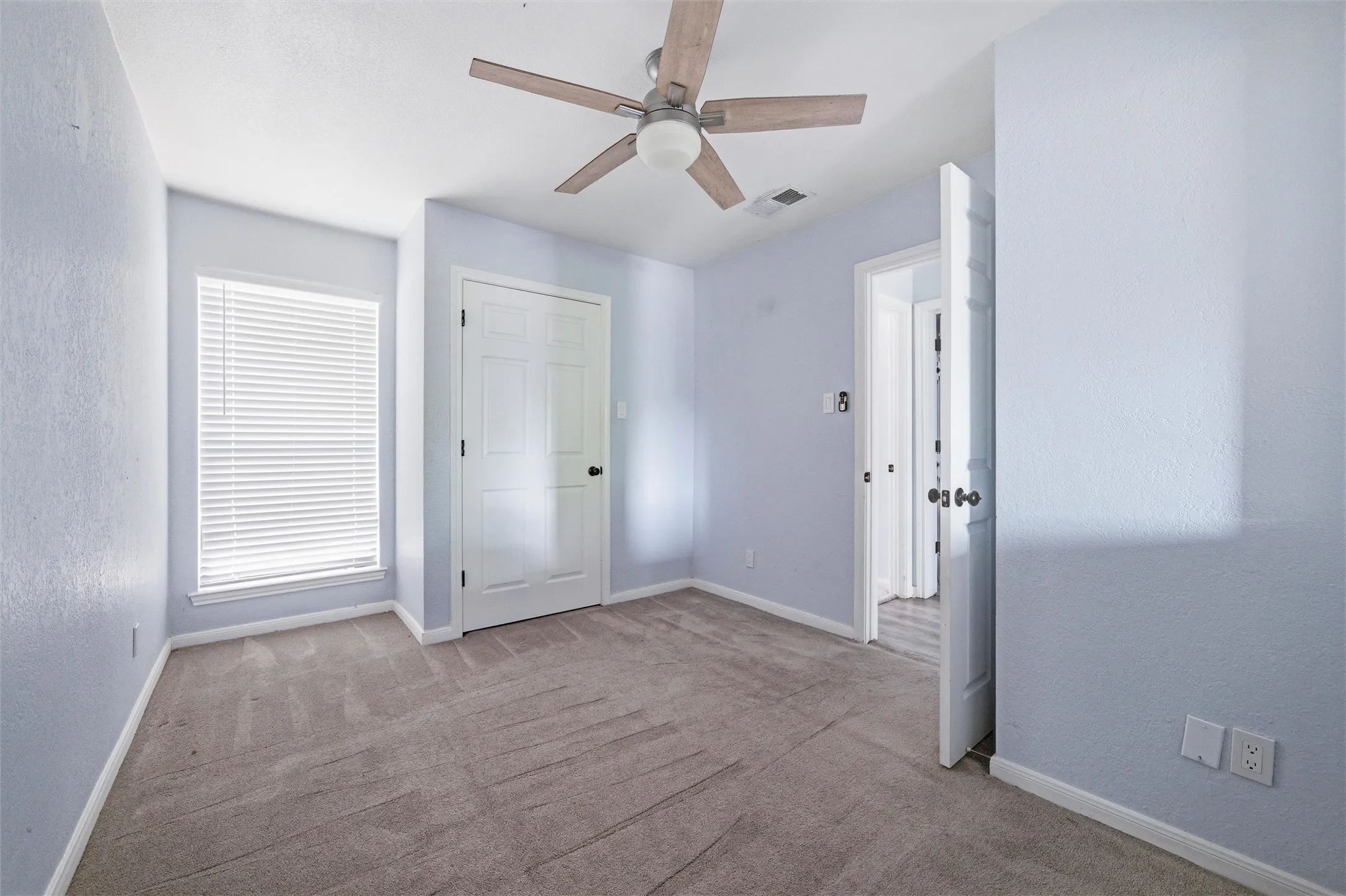 Carpeted room featuring a ceiling fan with wood-finish blades, a window with horizontal blinds, and a paneled closet door