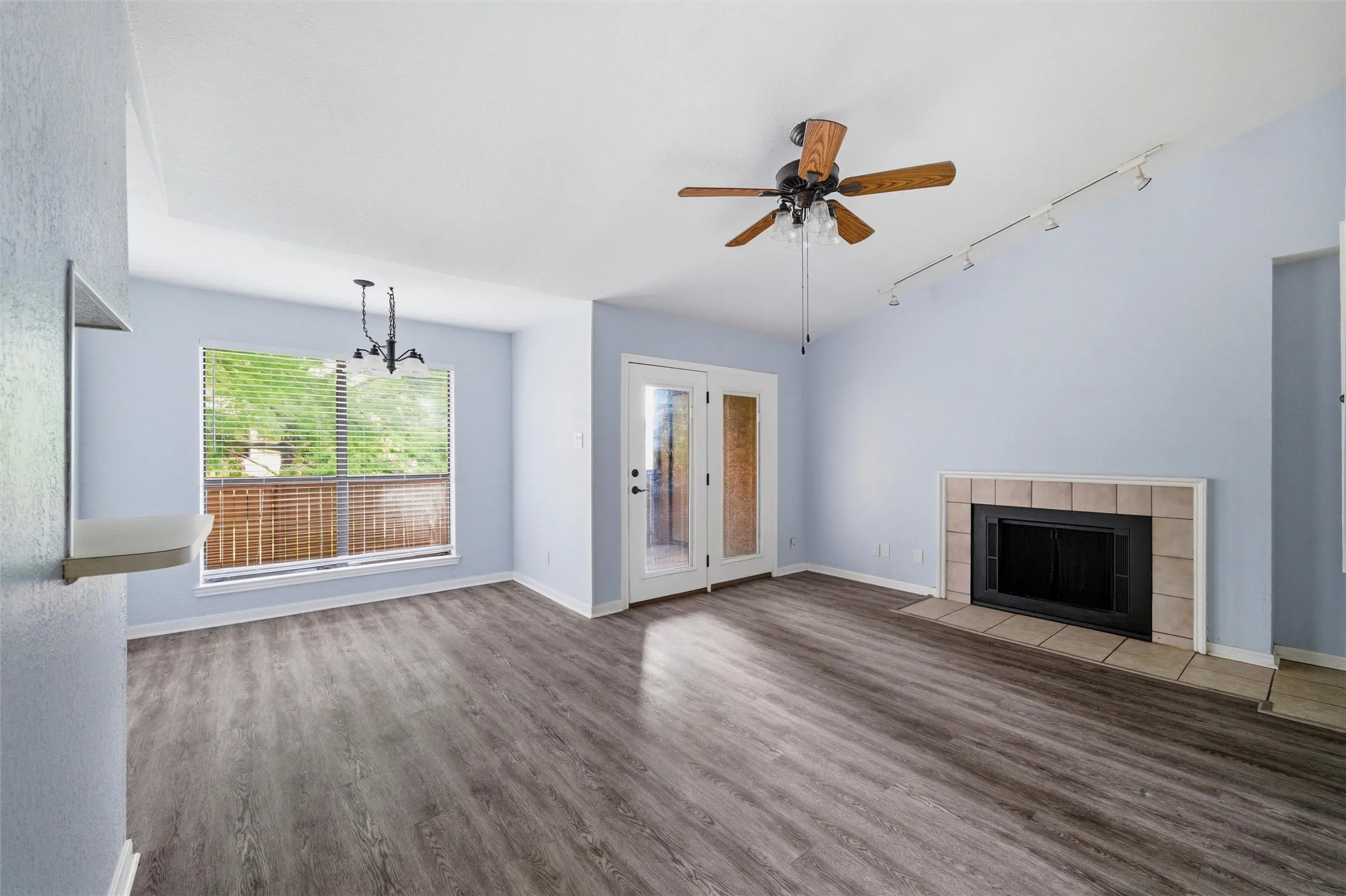 Spacious living area featuring wood-finish flooring, a fireplace with a tile surround, and vaulted ceilings