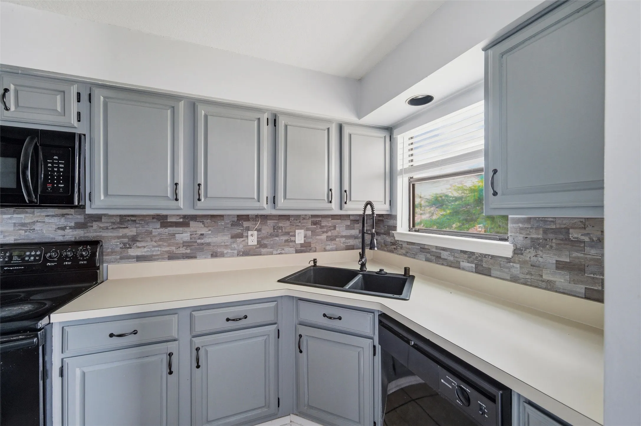 Kitchen featuring light gray cabinetry, a black double basin sink with a high-arc faucet, and a stone-style backsplash