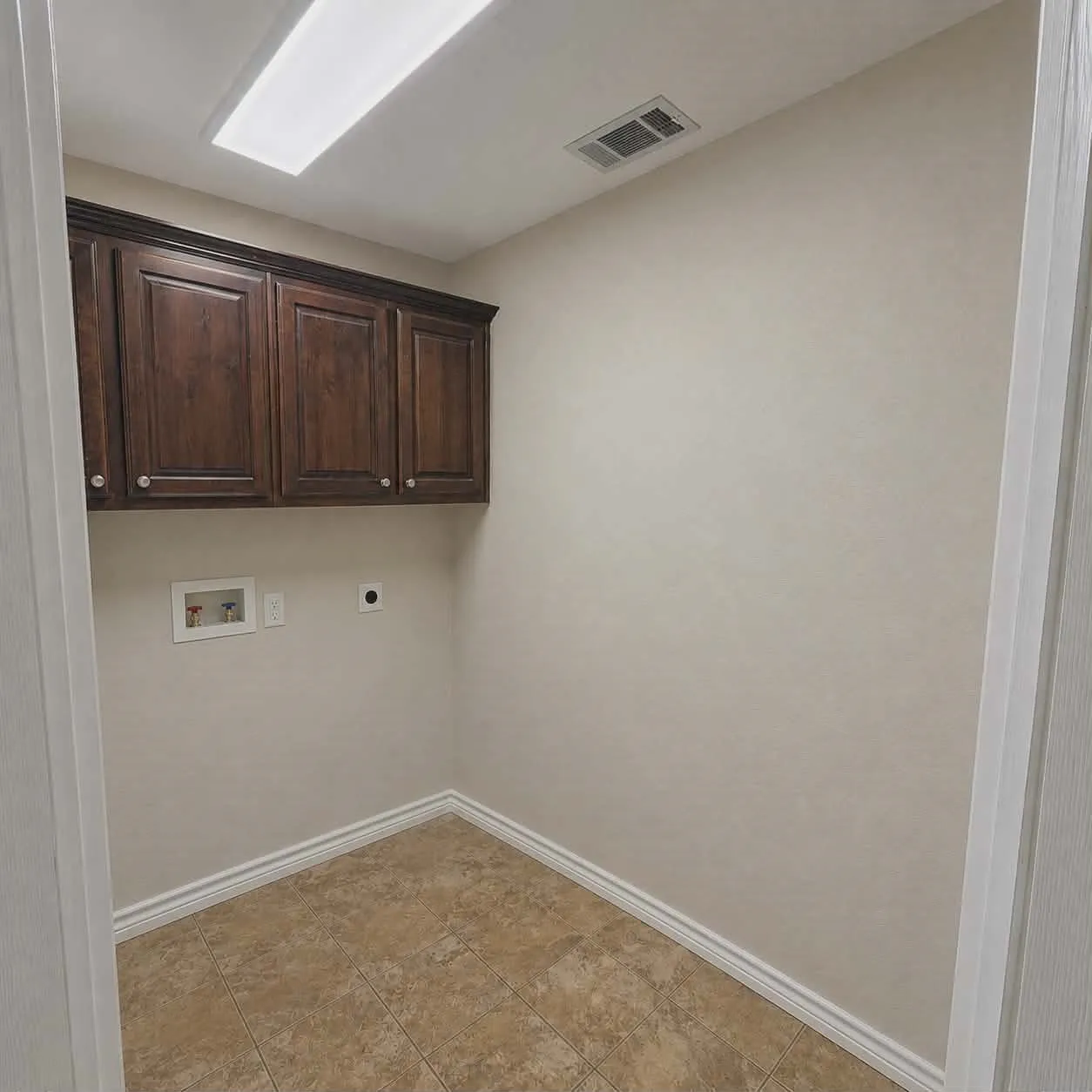 Utility space featuring rich wood-finish cabinetry, ceramic tile flooring, and a flush-mount overhead light-This photo was taken before family moved in