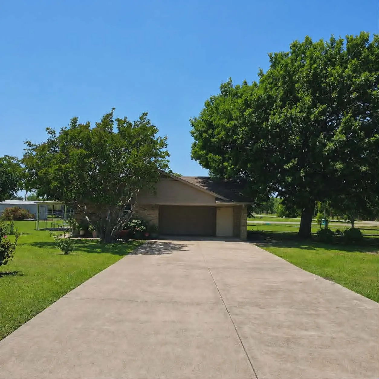 Ranch-style exterior with a two-car garage, concrete driveway, and mature landscaping