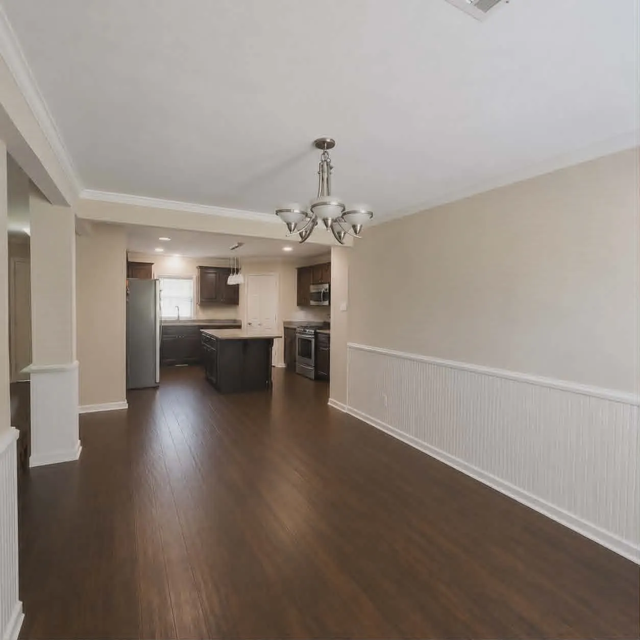 Dining area -Expansive room featuring wood-finish flooring, wainscoting, and a five-light chandelier-This photo was taken before family moved in