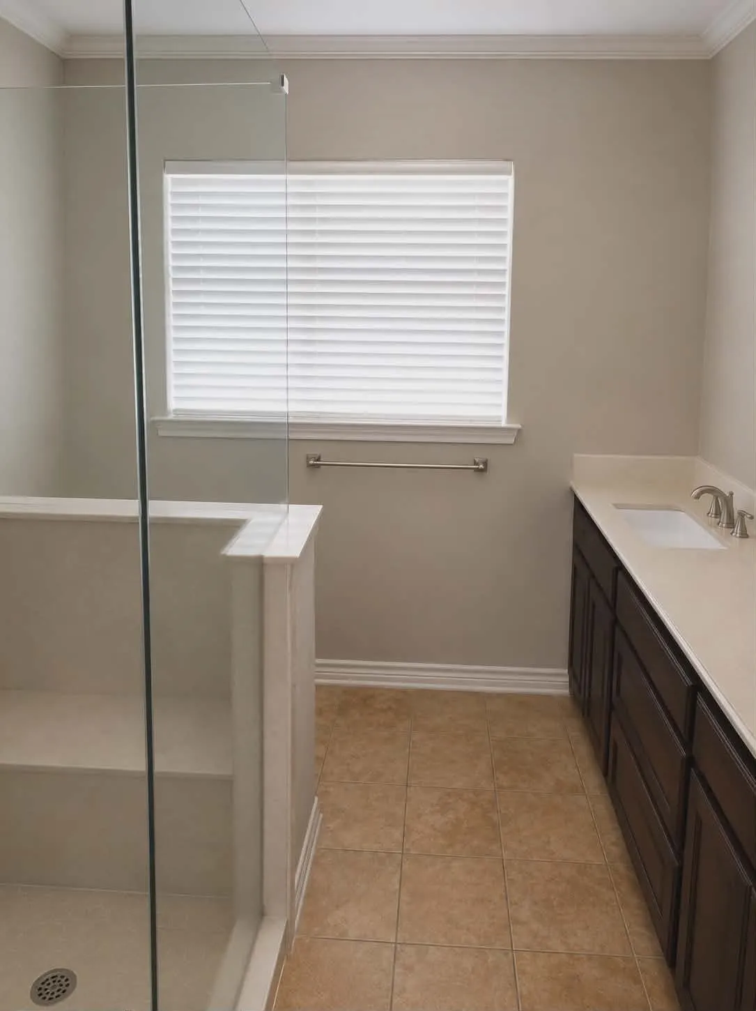 Bathroom featuring a glass-enclosed shower with integrated shelving, a dark wood-finish vanity with an undermount sink, a light-toned countertop, and tiled flooring-This photo was taken before family moved in