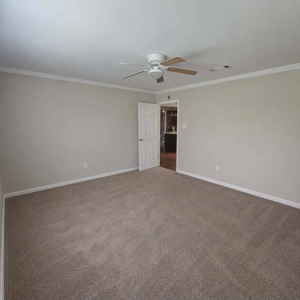 Spacious room featuring neutral carpeting, light-toned wall paint, crisp white trim, and a ceiling fan with wood-finish blades-This photo was taken before family moved in