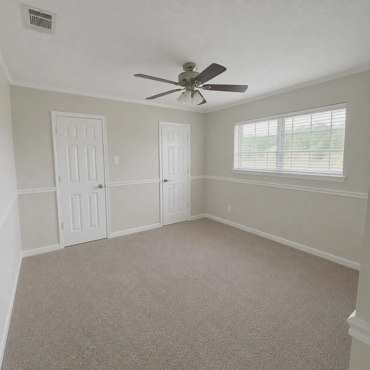 Bedroom 3- Spacious room with two closets featuring neutral carpeting, a ceiling fan, crown molding, and wainscoting-This photo was taken before family moved in