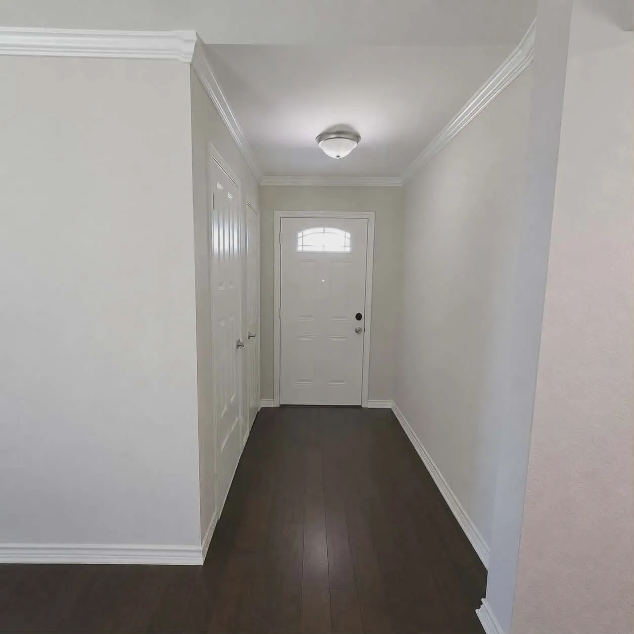 Main front door- Entryway featuring a white exterior door with an arched window, rich wood-finish flooring, and crown molding