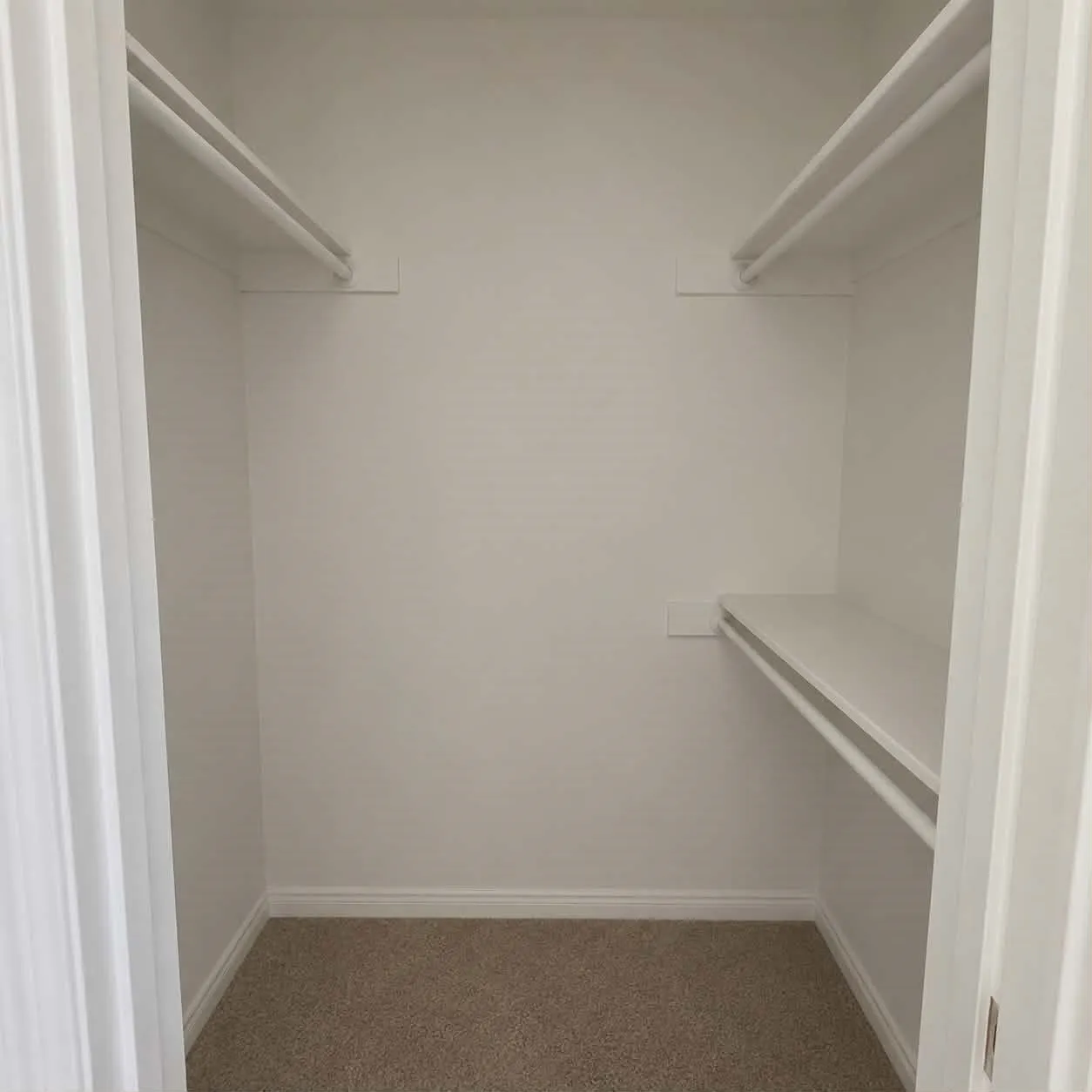 Bedroom 2-Neutral-toned carpeted closet featuring white shelving and hanging rods-This photo was taken before family moved in