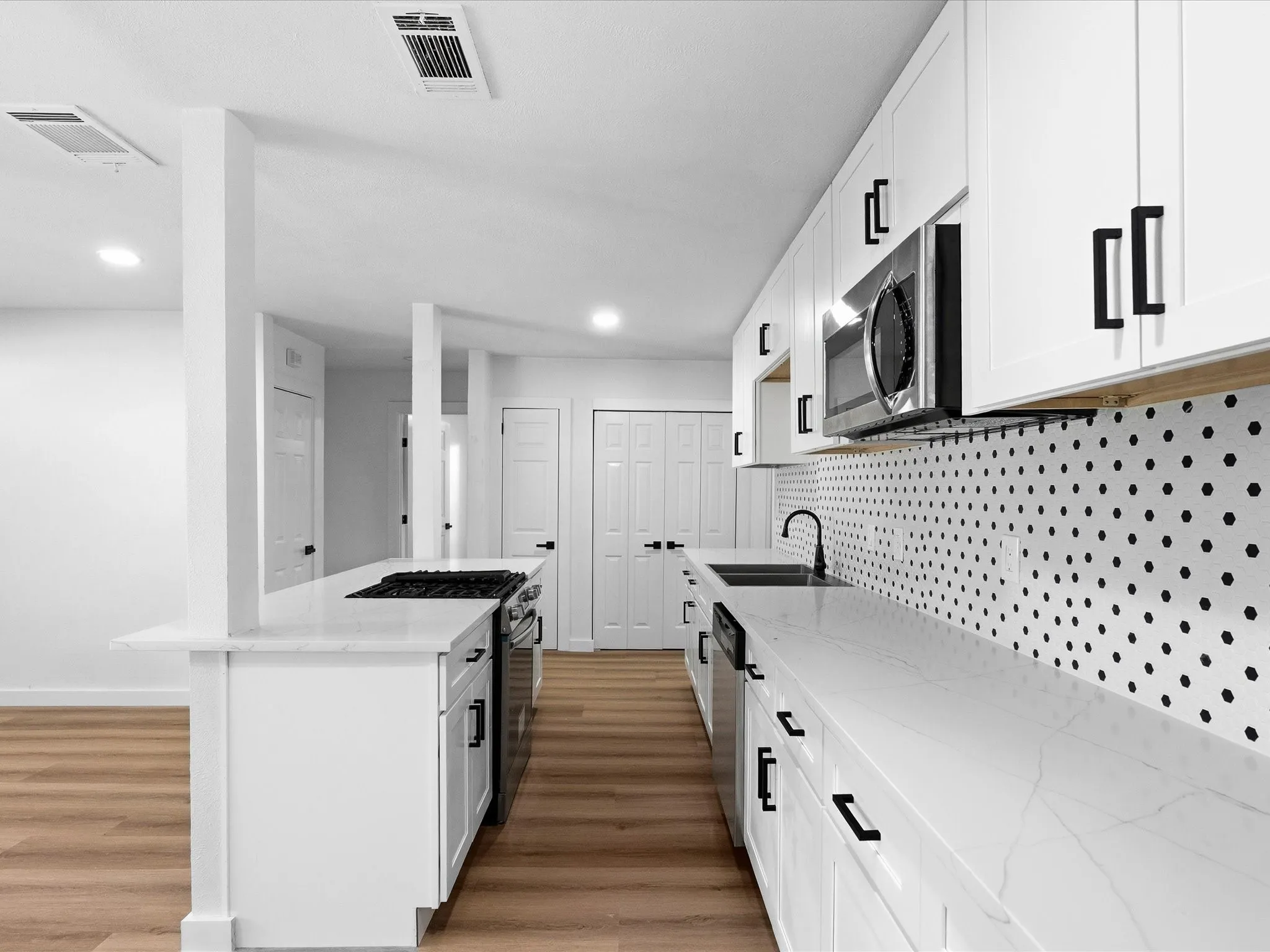 Modern kitchen featuring white cabinetry with black hardware, stainless steel appliances, white countertops, and wood-finish flooring
