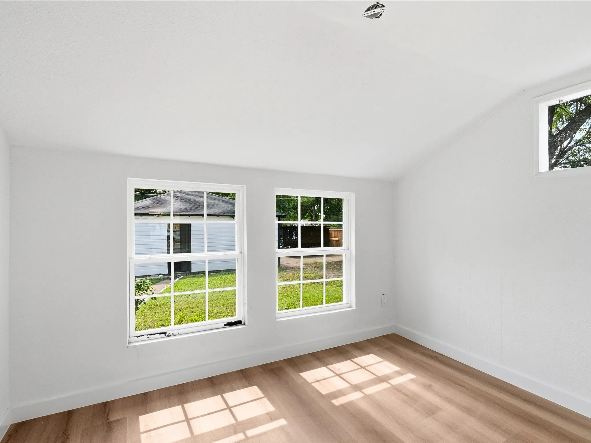 Interior room featuring a vaulted ceiling, white walls, and wood-finish flooring
