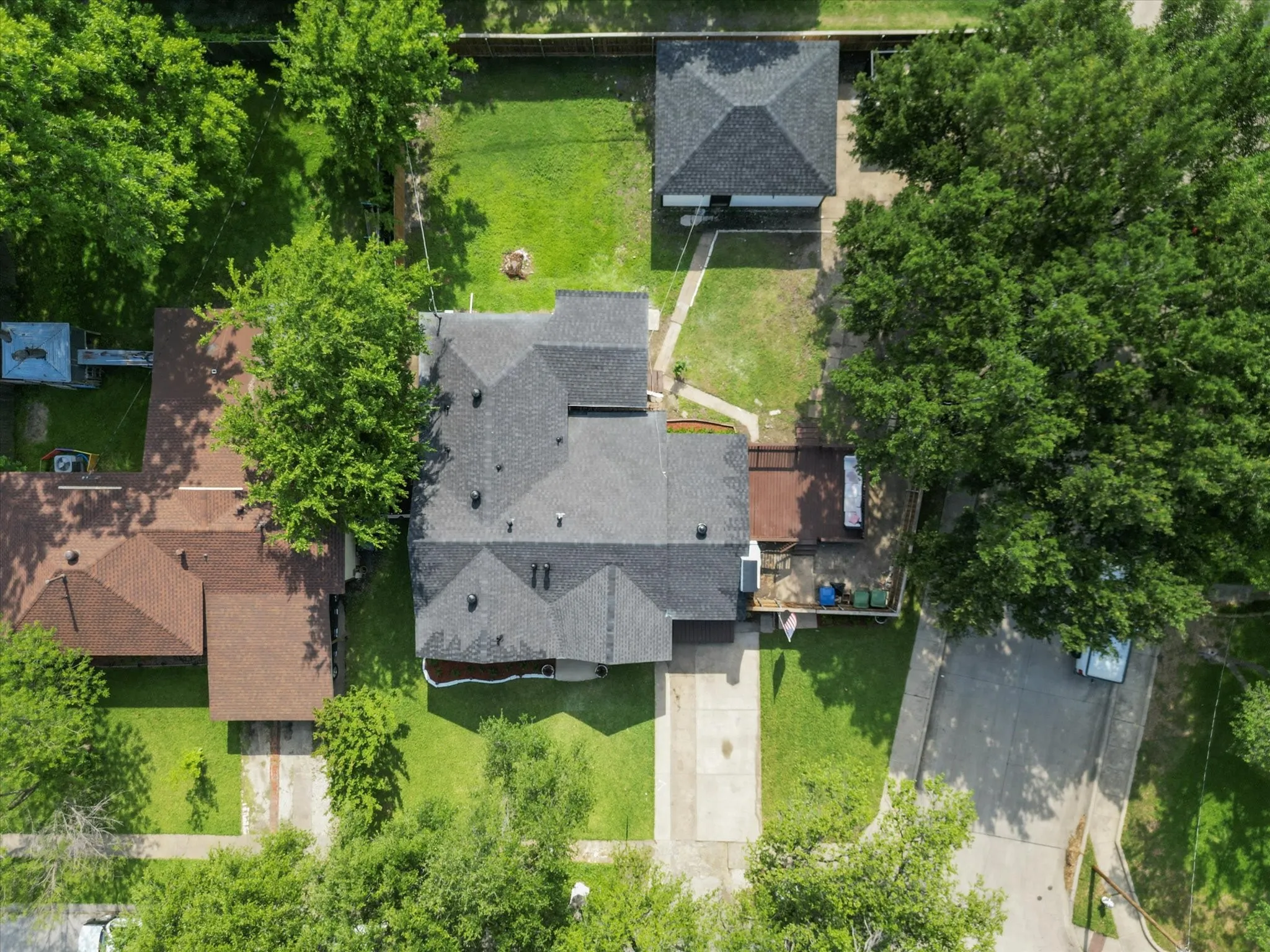 Expansive property featuring a main residence with a dark shingle roof, a detached garage with a matching dark shingle roof, a concrete driveway, a rear deck, and mature trees throughout the lot
