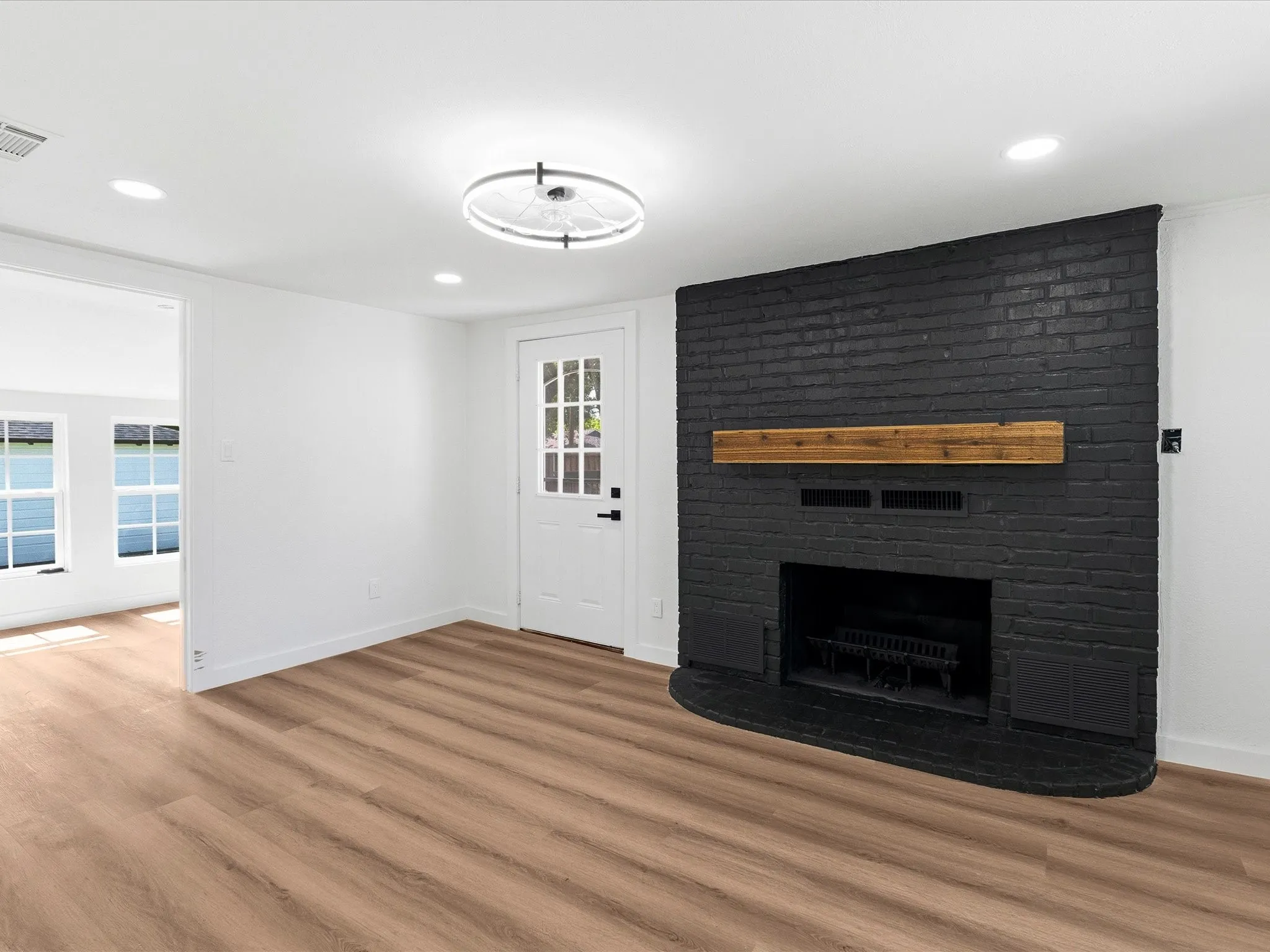 Living area featuring a black brick fireplace with a wood mantle, wood-finish flooring, recessed lighting, and a modern circular light fixture