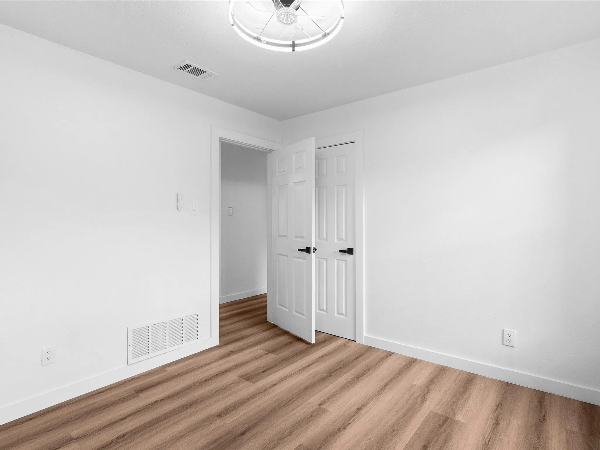 Spacious room featuring wood-finish flooring, white baseboards, and a contemporary ceiling light fixture