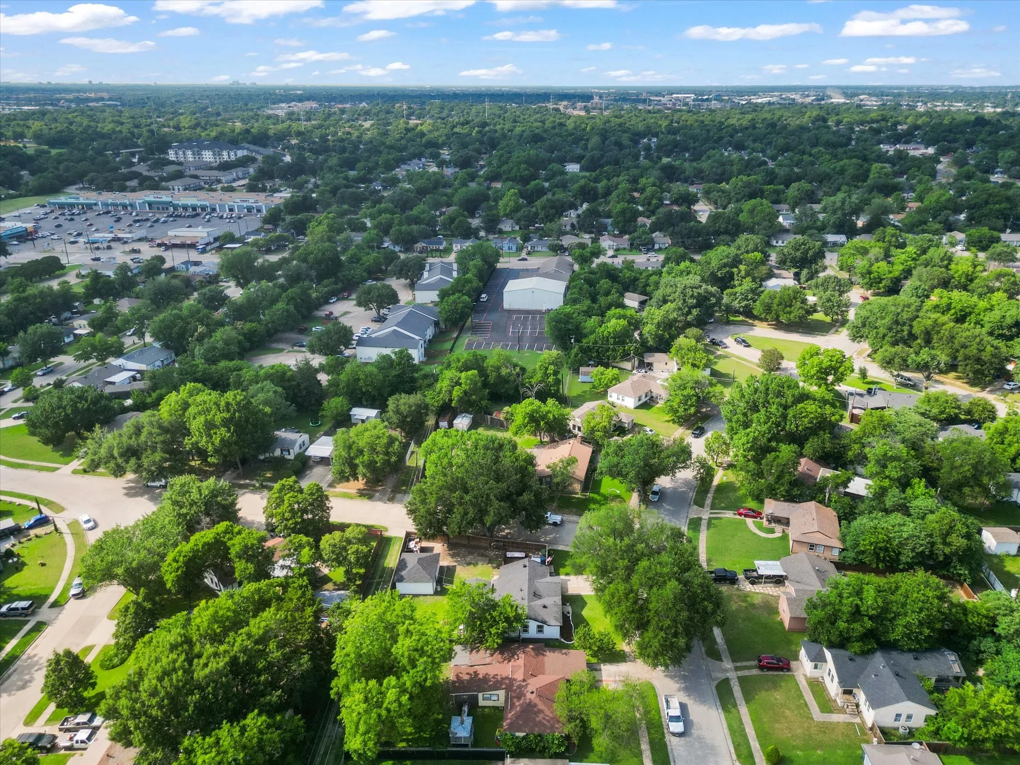 Aerial perspective showcasing a residential area with extensive tree canopy, paved streets, and a mix of single-story homes