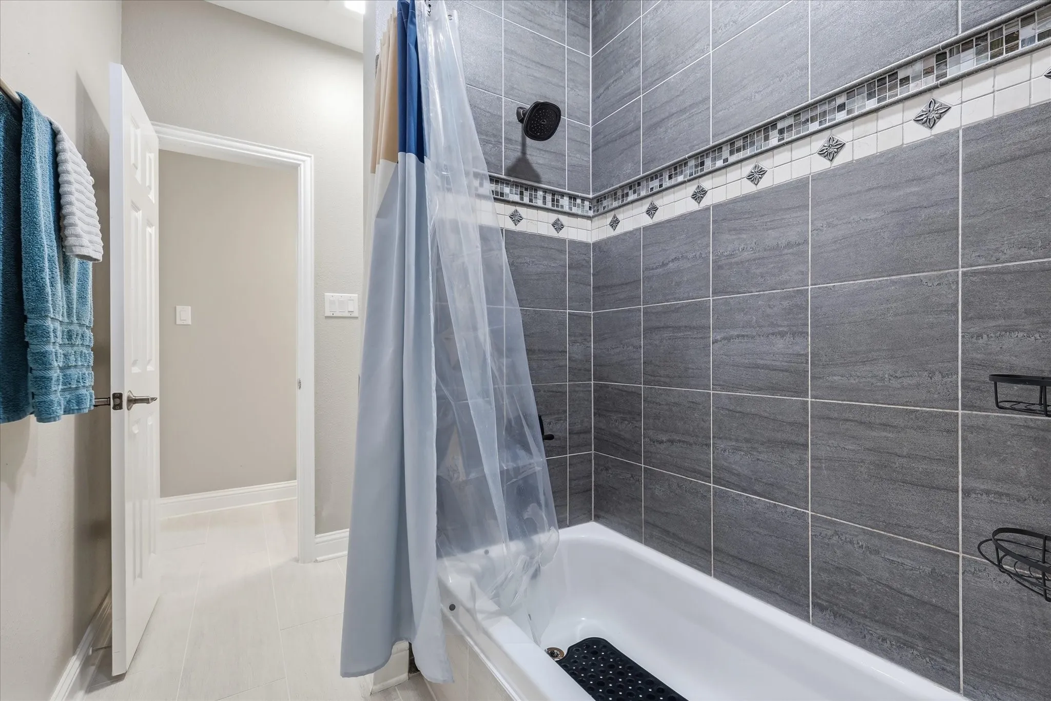 Full bathroom featuring a white bathtub, dark gray stone-look wall tiles, and a decorative mosaic tile accent band