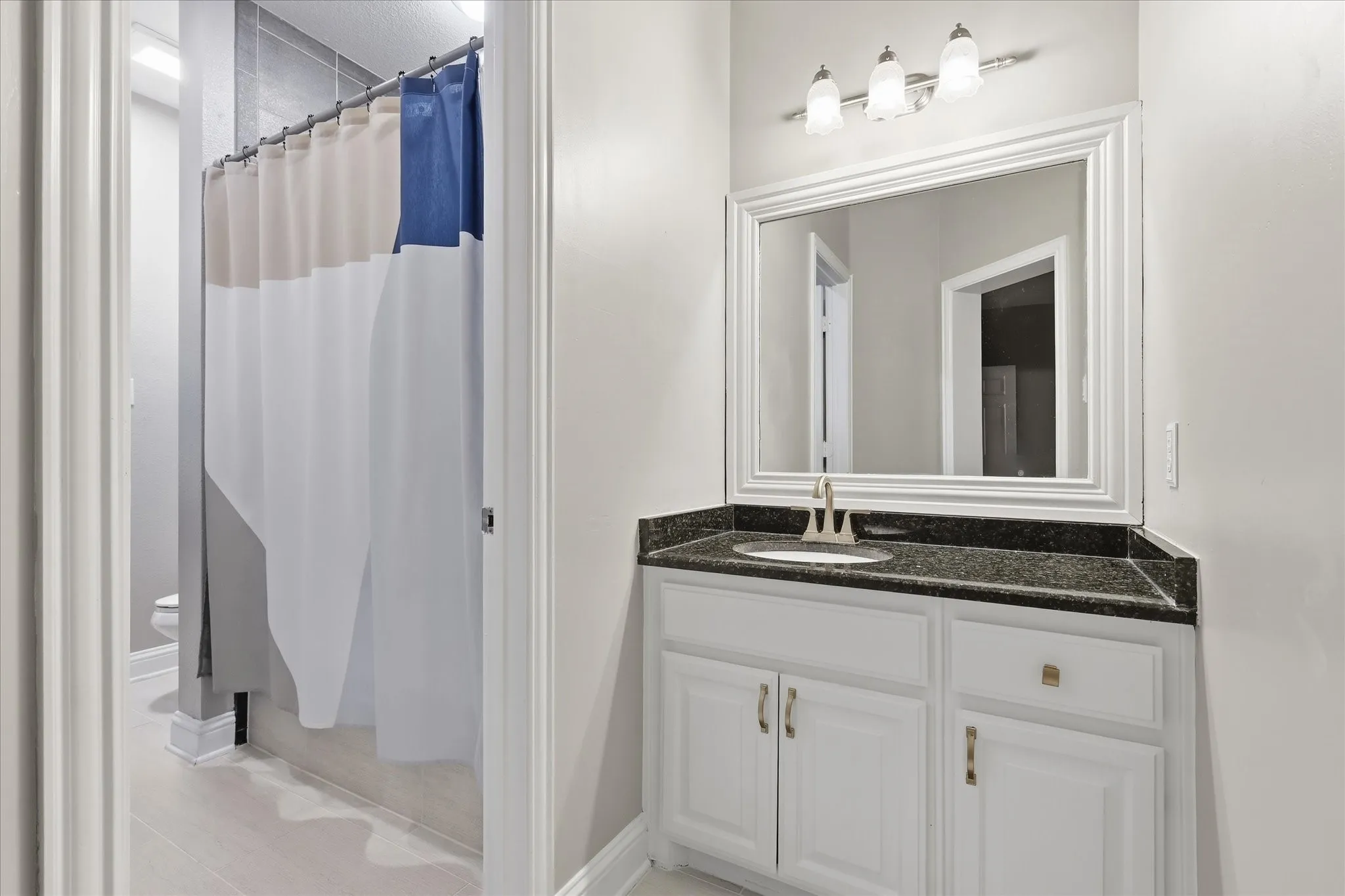 Bathroom vanity featuring a dark speckled countertop, an undermount sink, and a framed mirror