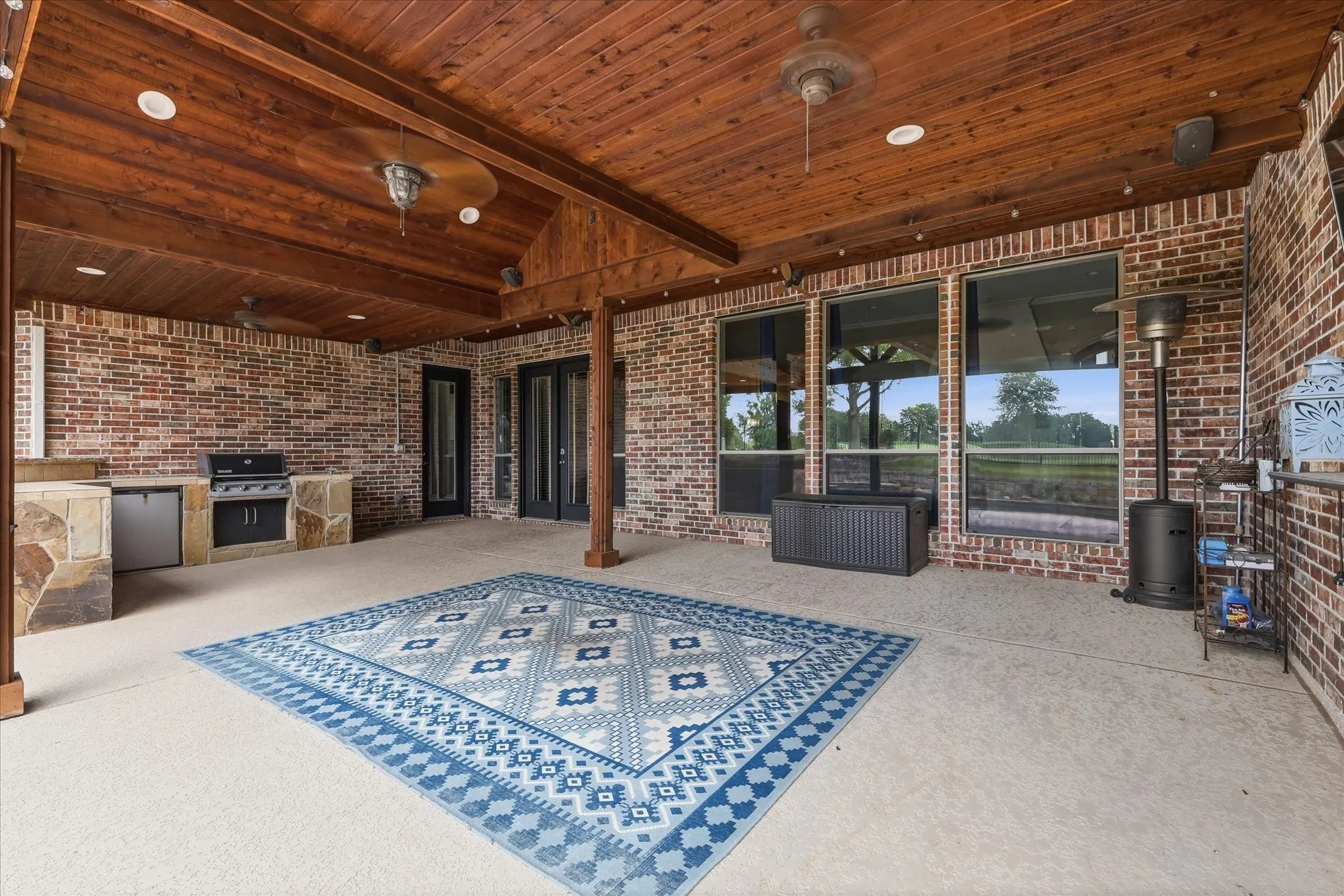 Expansive covered patio featuring a wood-plank ceiling, exposed brick walls, and an outdoor kitchen with built-in grill and refrigerator