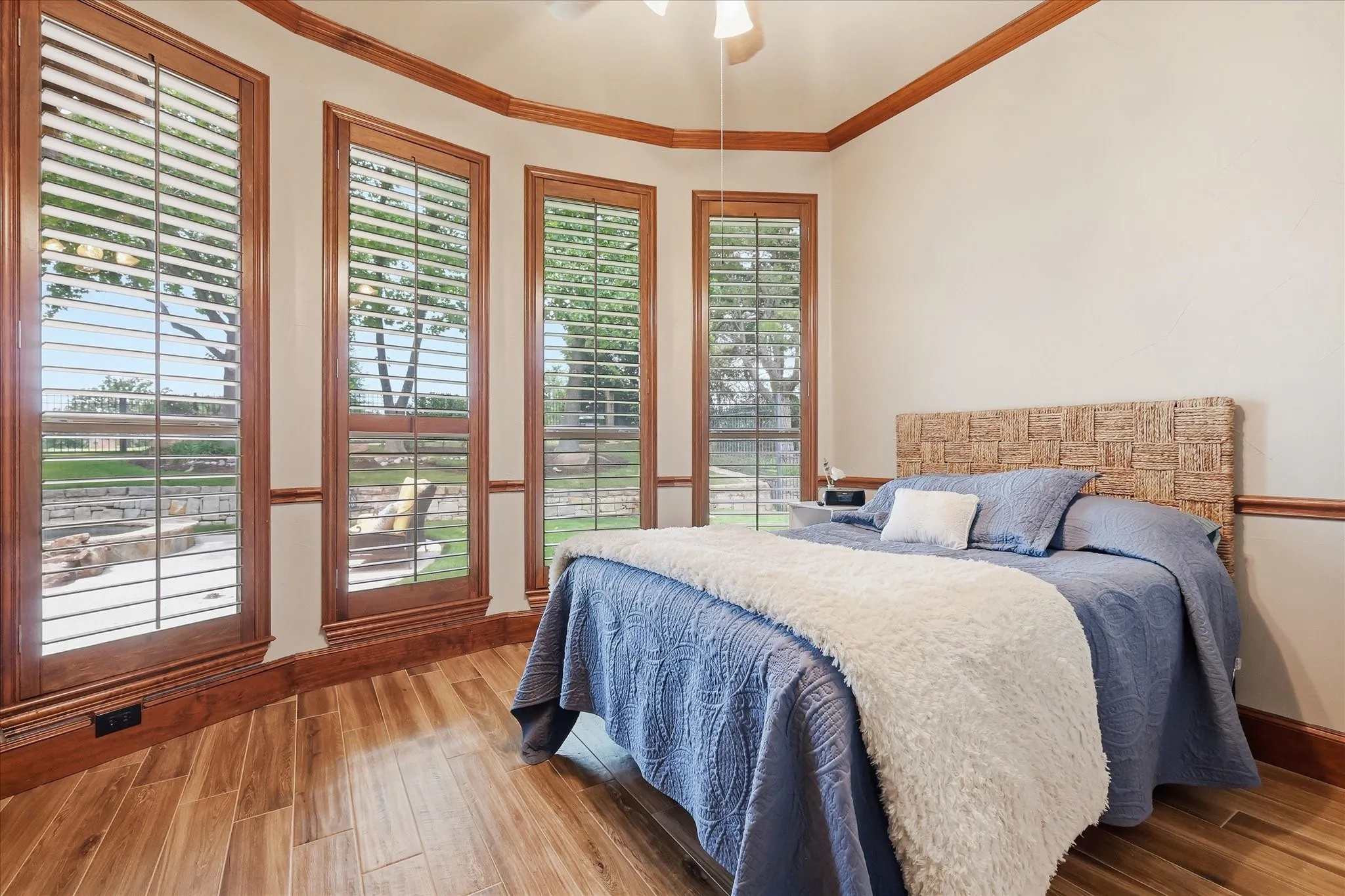 Spacious room featuring multiple tall windows with plantation shutters, wood-finish flooring, and crown molding