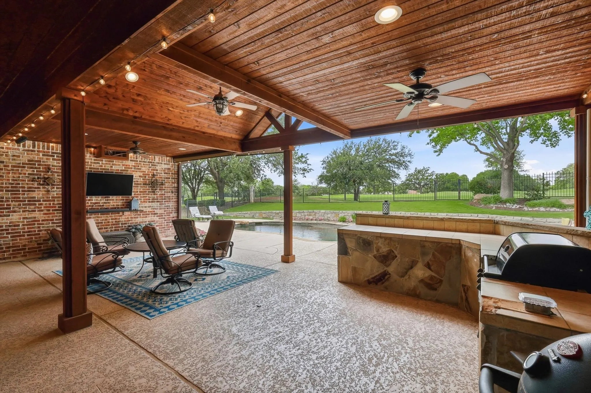 Expansive covered patio featuring a wood-plank ceiling with exposed beams, recessed lighting, and ceiling fans